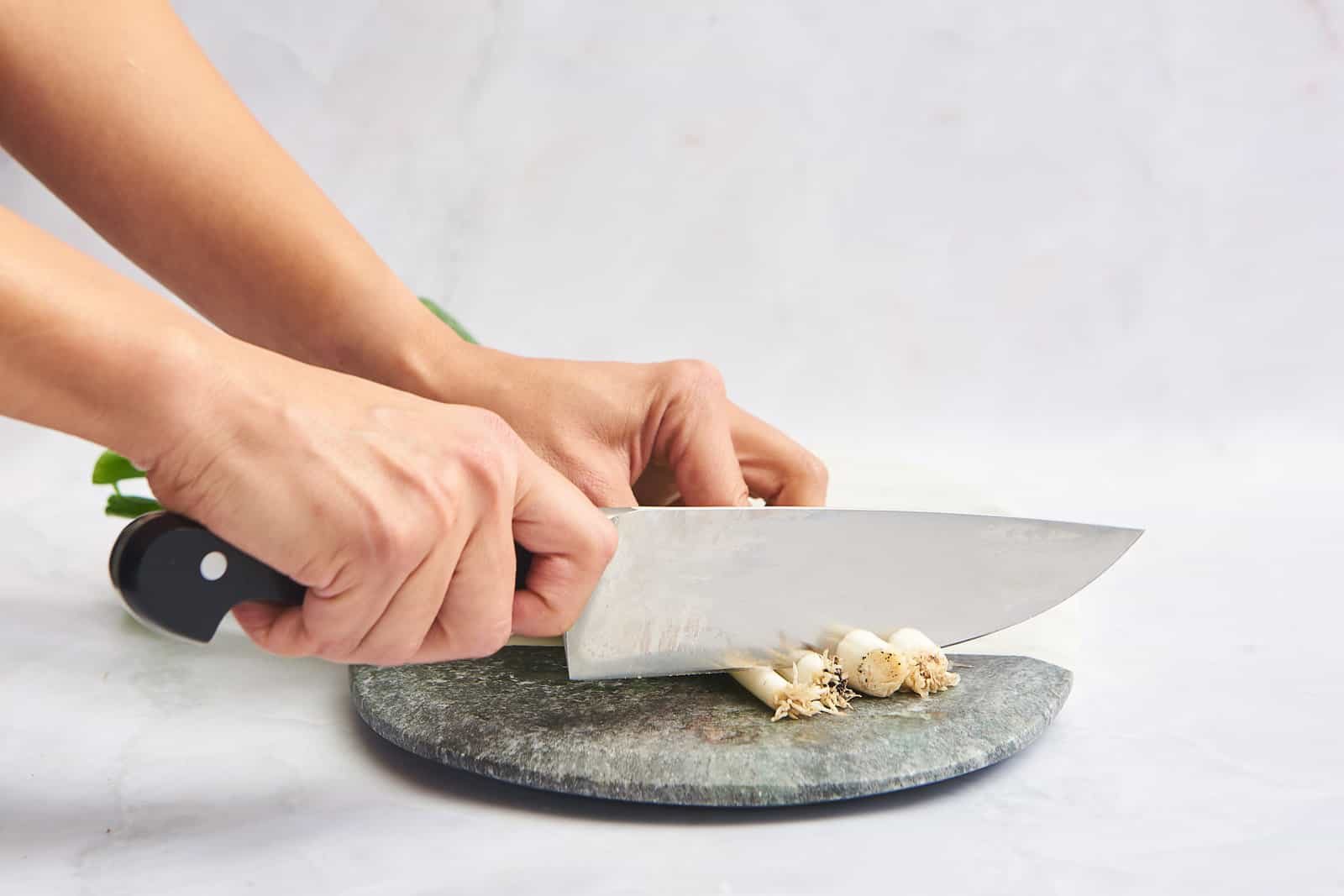 A hand trimming the roots off green onions.