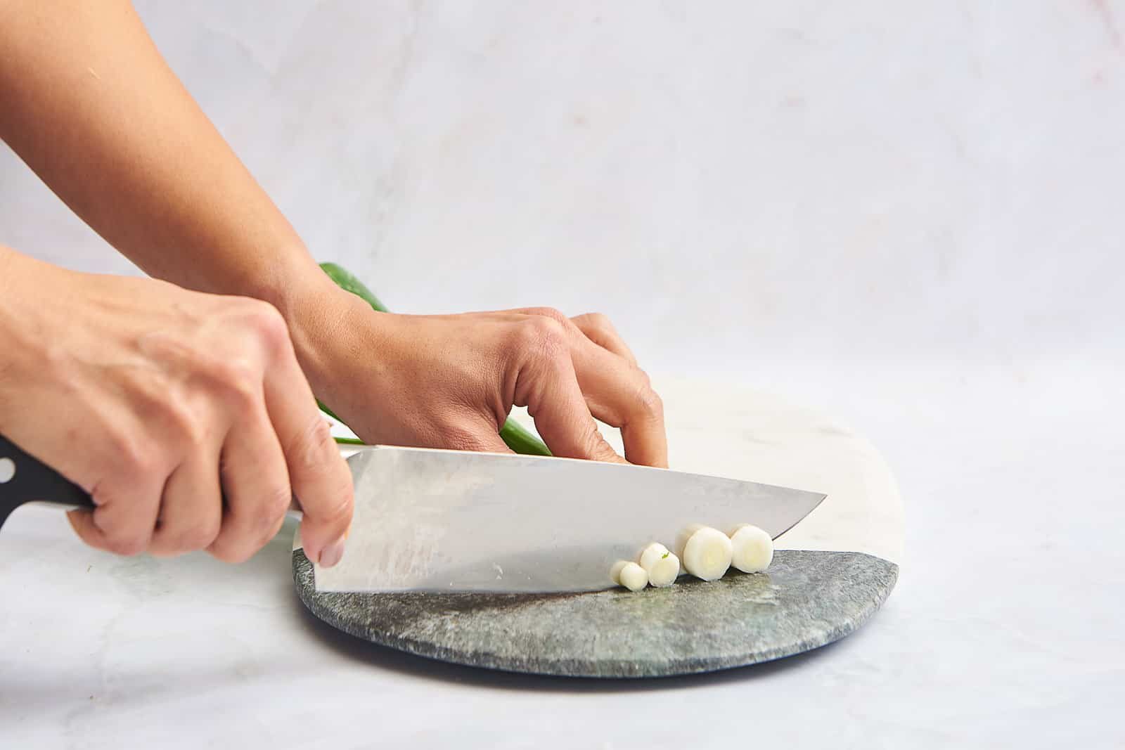Two hands chopping the white ends of green onions.