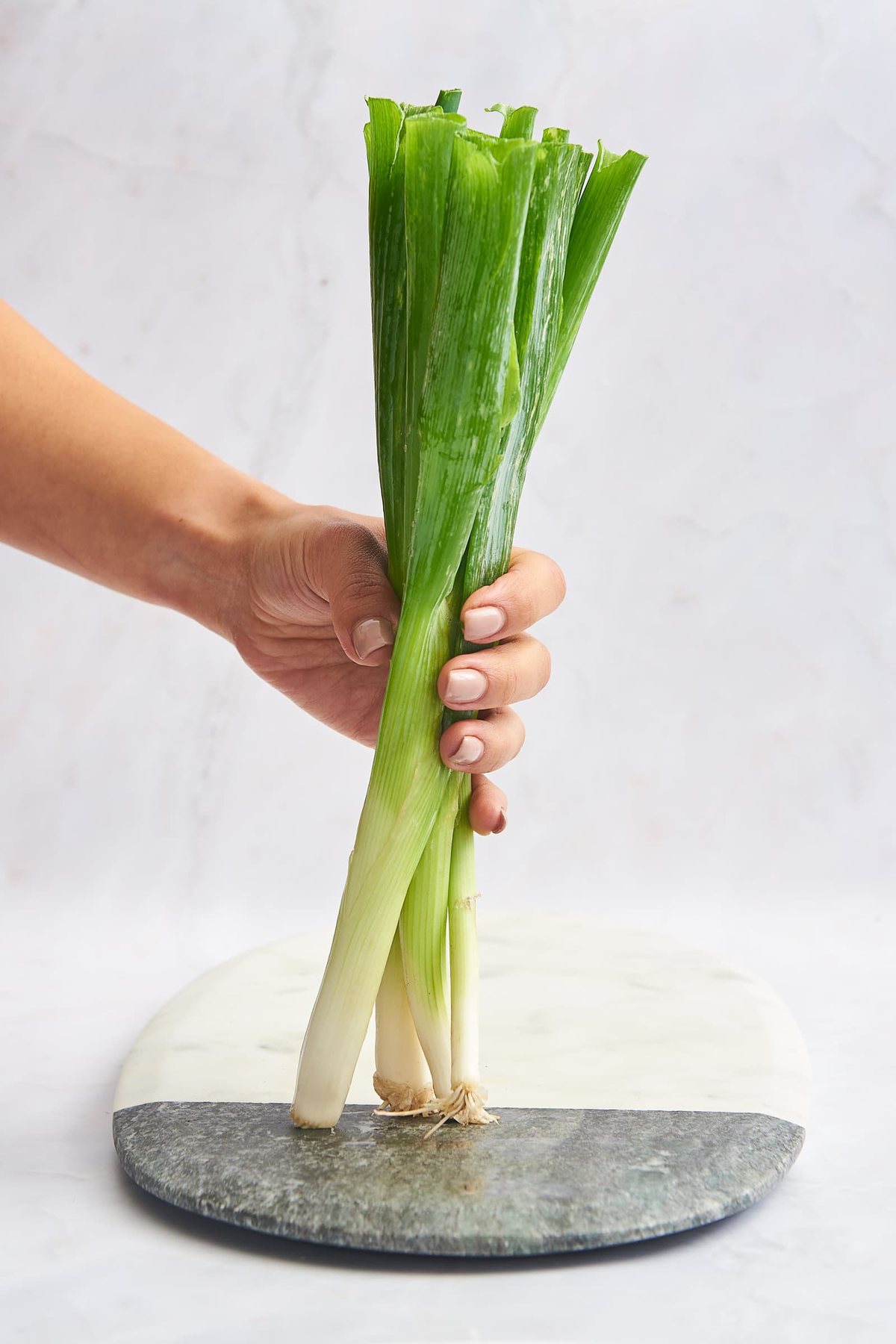 A hand holding a bunch of green onions on a cutting board.