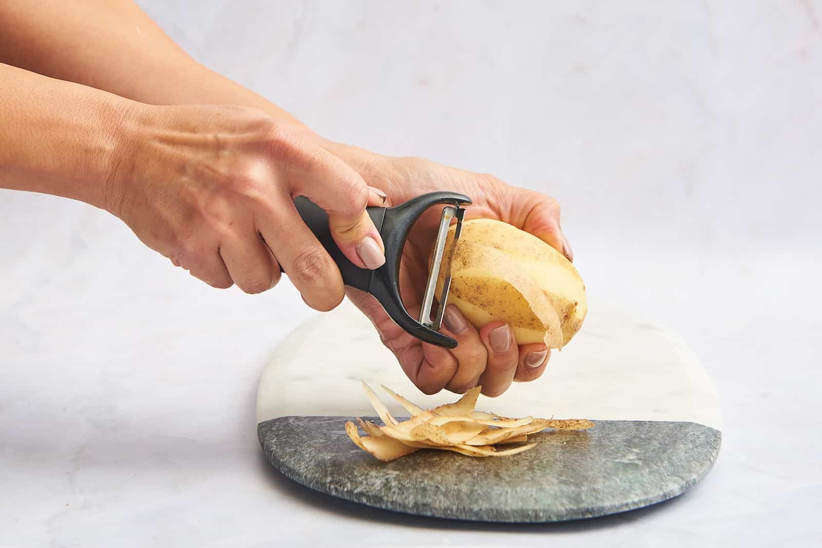 A potato being peeled with a vegetable peeler.