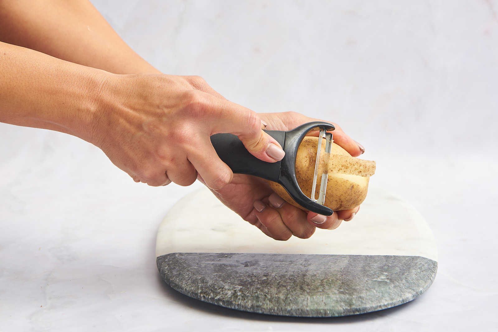 A potato being peeled with a vegetable peeler.