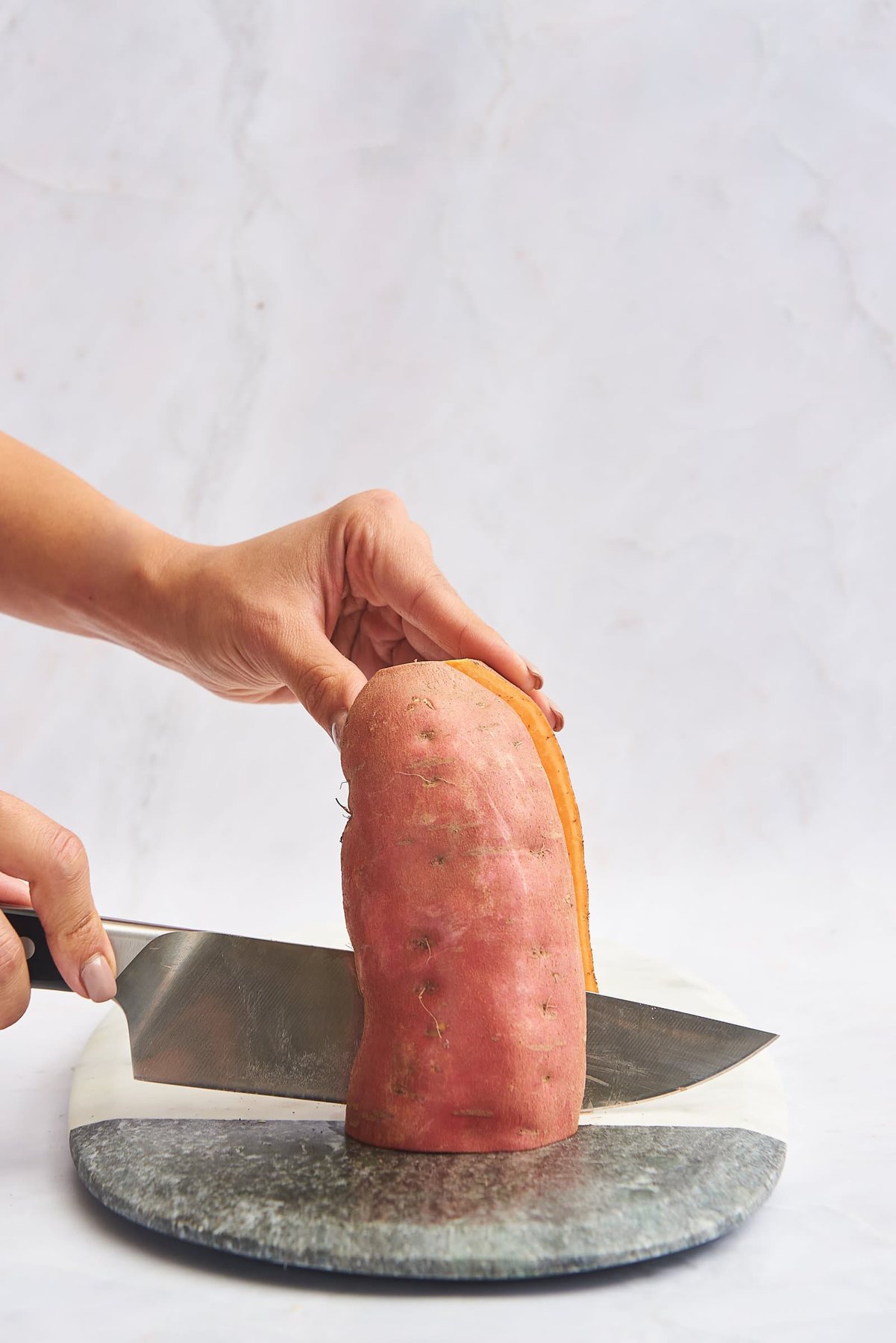 A sweet potato being sliced in half lengthwise.