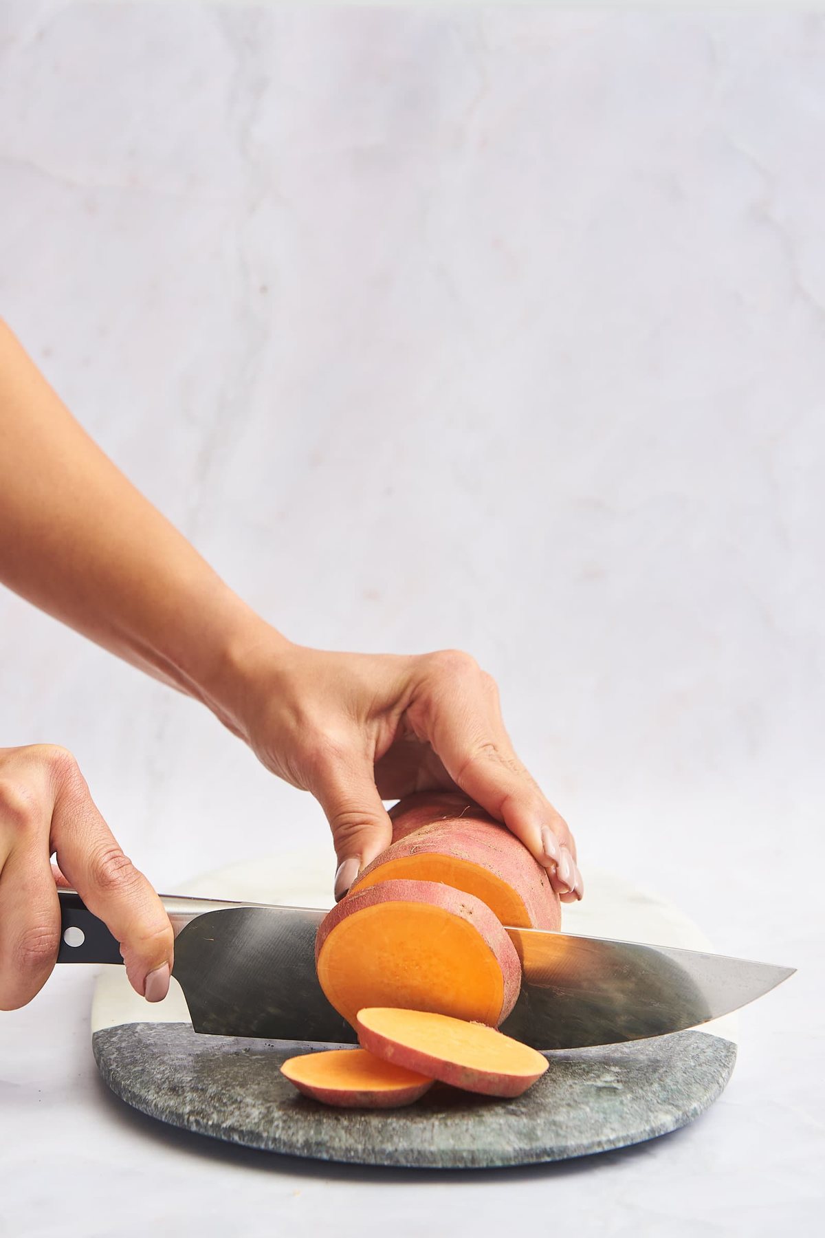 A sweet potato being sliced into rounds.