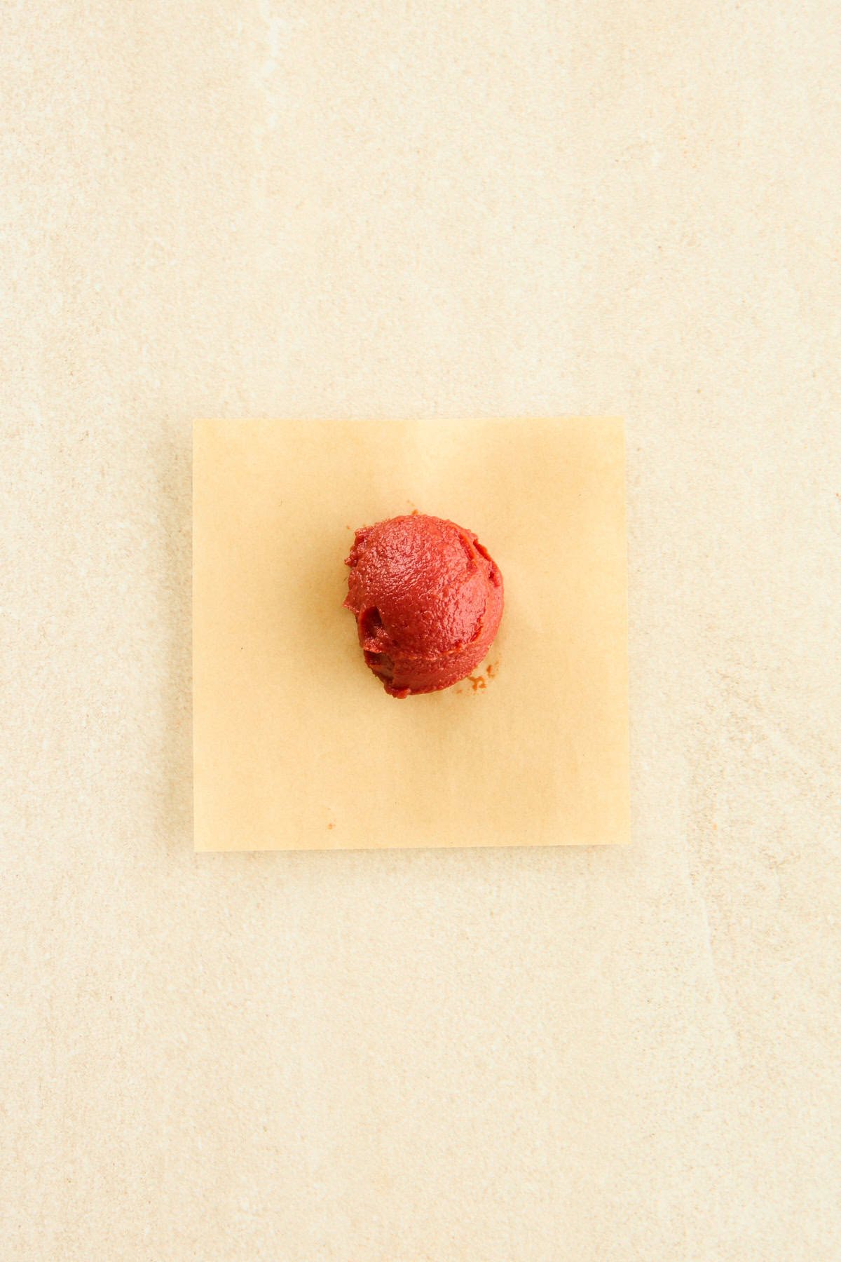 A tablespoon of tomato paste on a sheet of parchment paper.