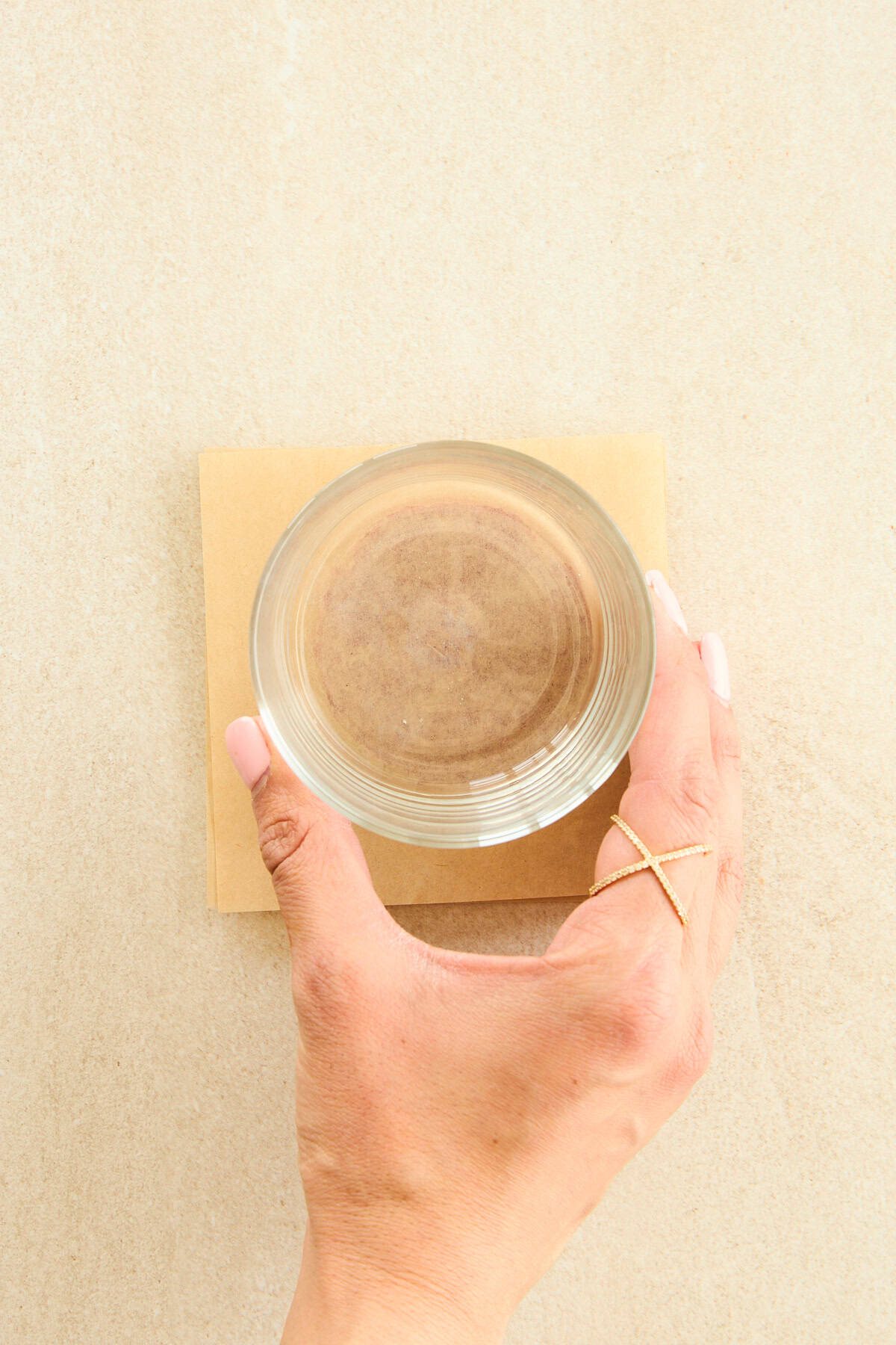 A cup being used to flatten tomato paste between parchment paper sheets.