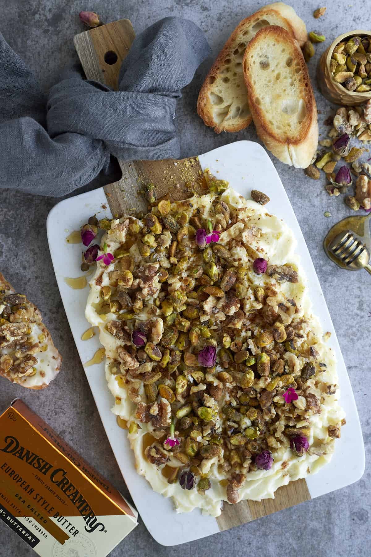 baklava butter on a white serving board surrounded by butter, crostini, and chopped nuts