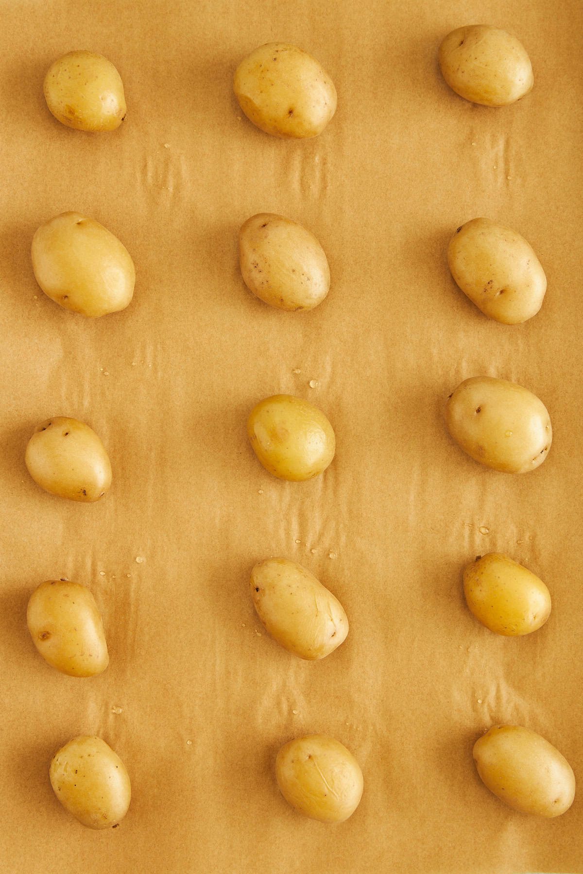 Boiled potatoes on a parchment paper lined baking sheet.