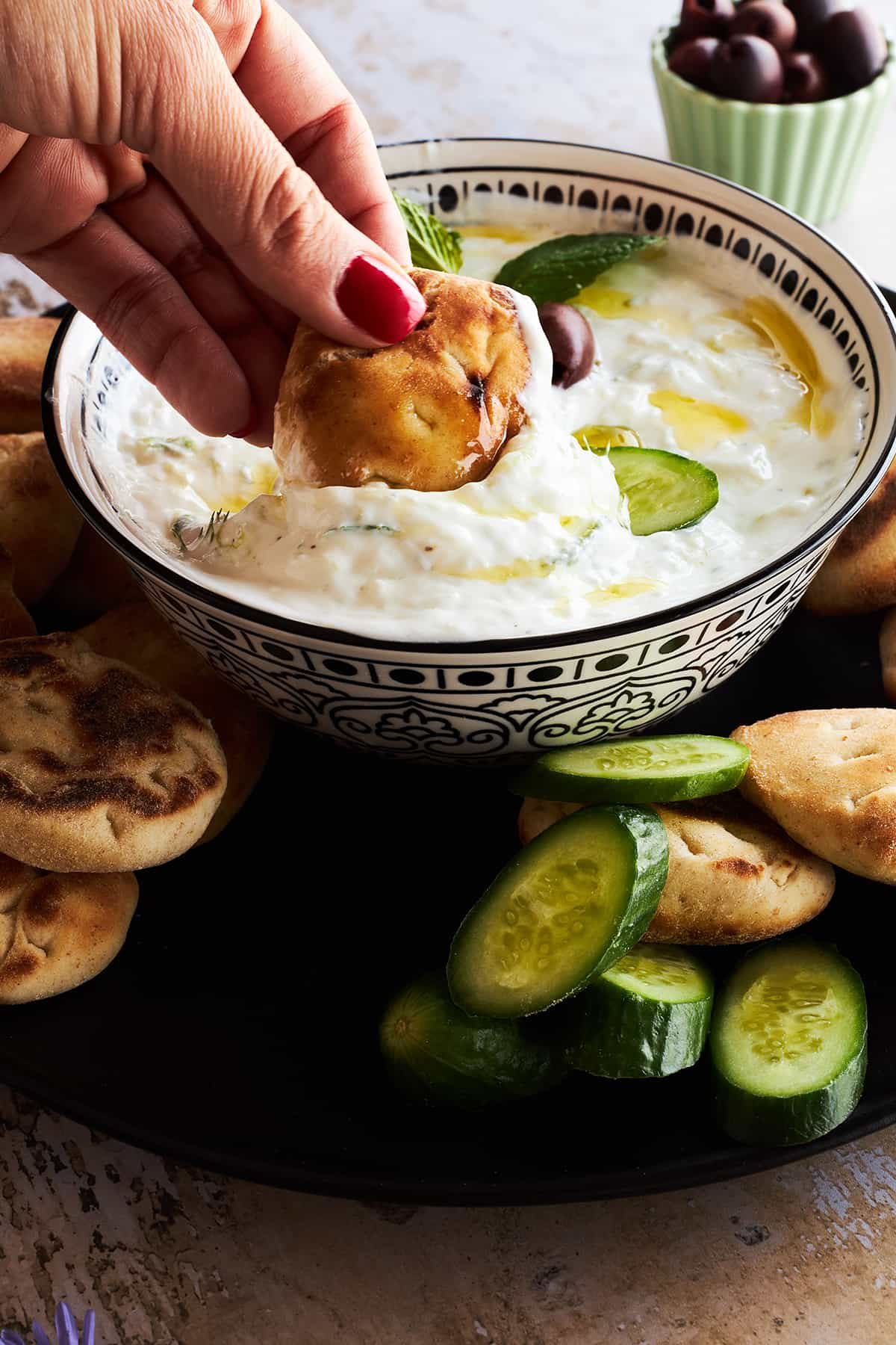 A hand dipping pita bread into a bowl of tzatziki sauce.