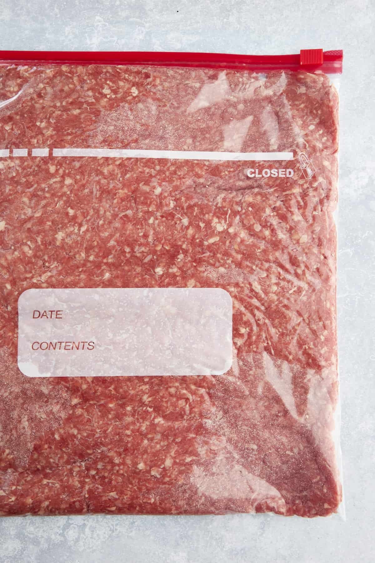 A flattened portion of uncooked ground beef in a sealable Ziploc bag.