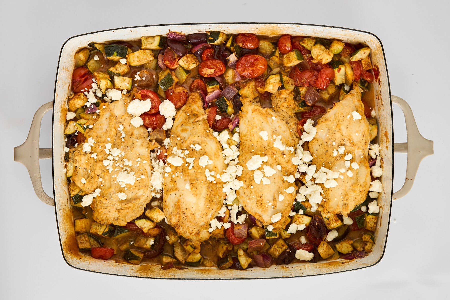Hummus baked chicken and veggies in a baking dish topped with feta.