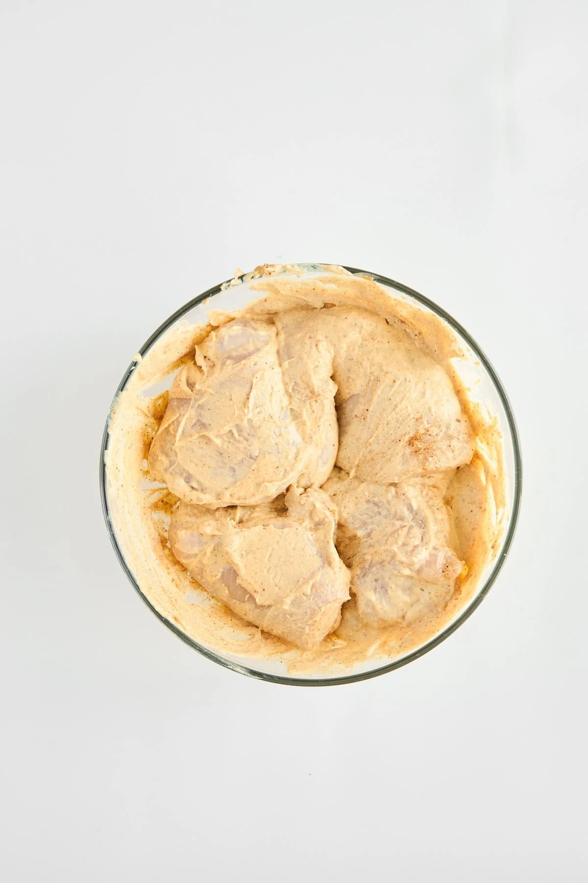 Raw chicken breasts marinating in a hummus mixture.