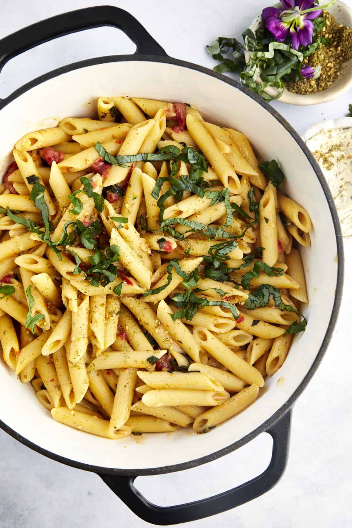 overhead image of cooked penne noodles with pimento peppers and seasonings in a pot