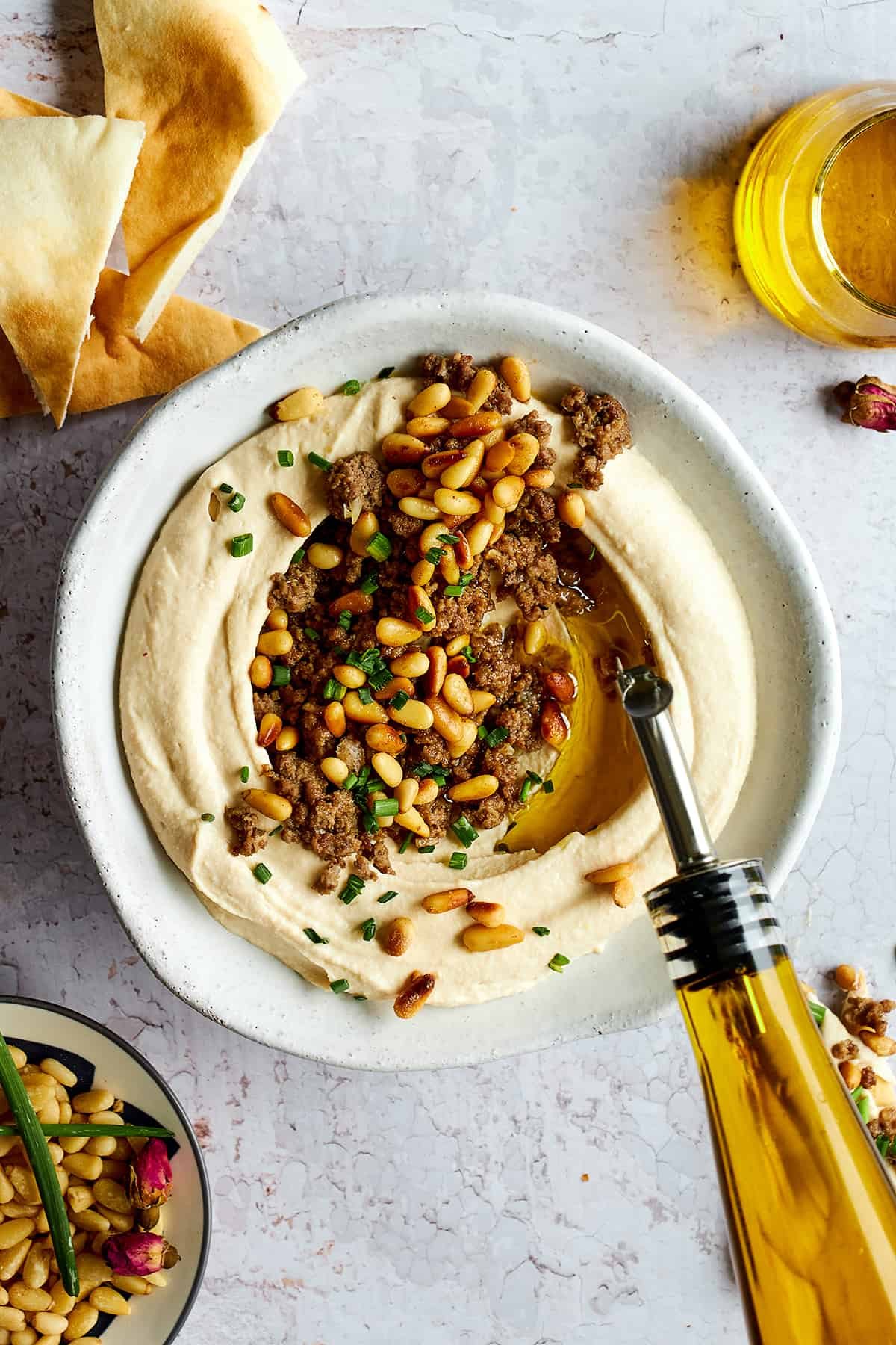 Olive oil being drizzled over a bowl of hummus with ground beef.