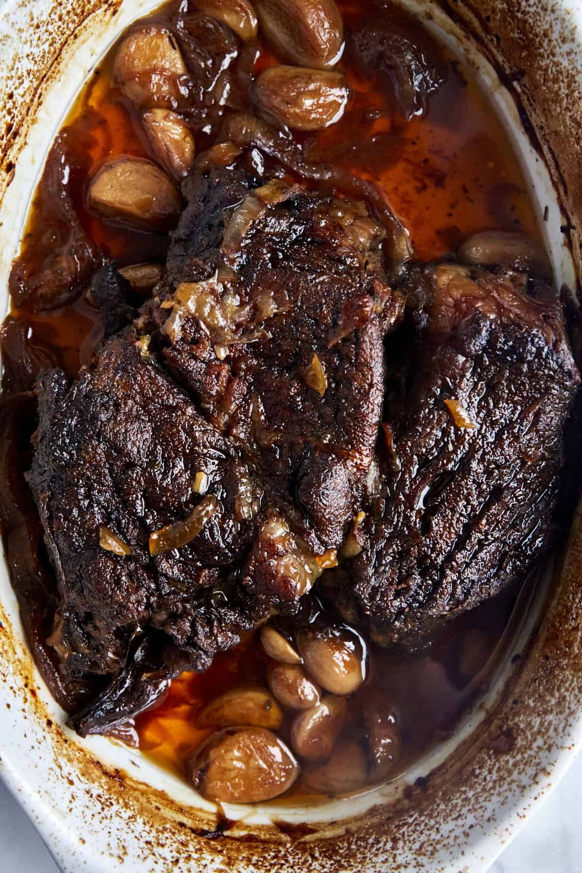 Whole roasted pot roast in a baking dish with onions and garlic.
