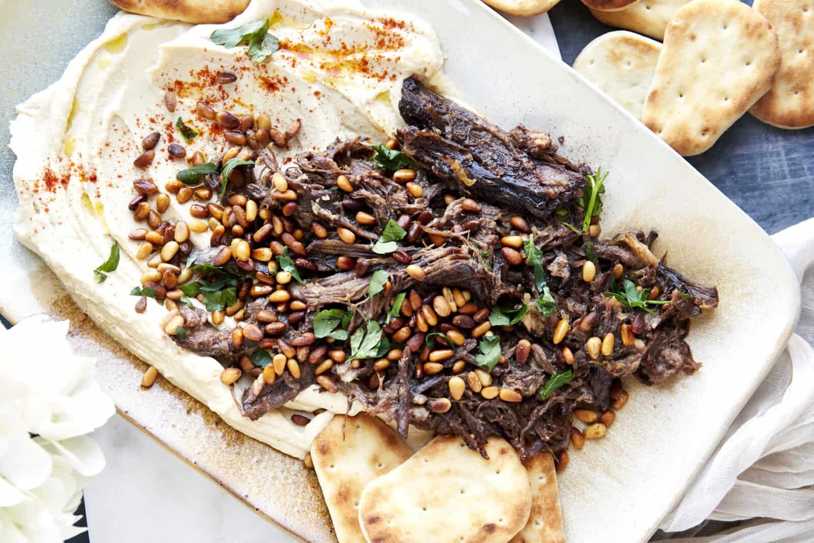 A platter with hummus topped with shredded pot roast meat, toasted pine nuts, and parsley.