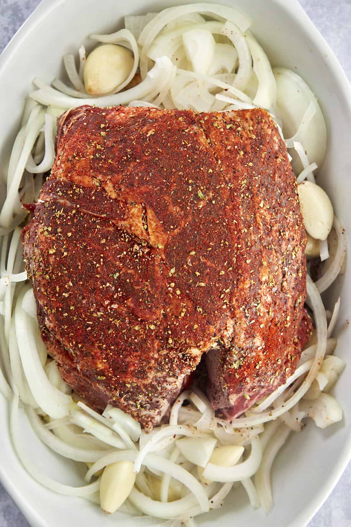 Raw chuck roast seasoned and placed on top of onions and garlic in a baking dish.