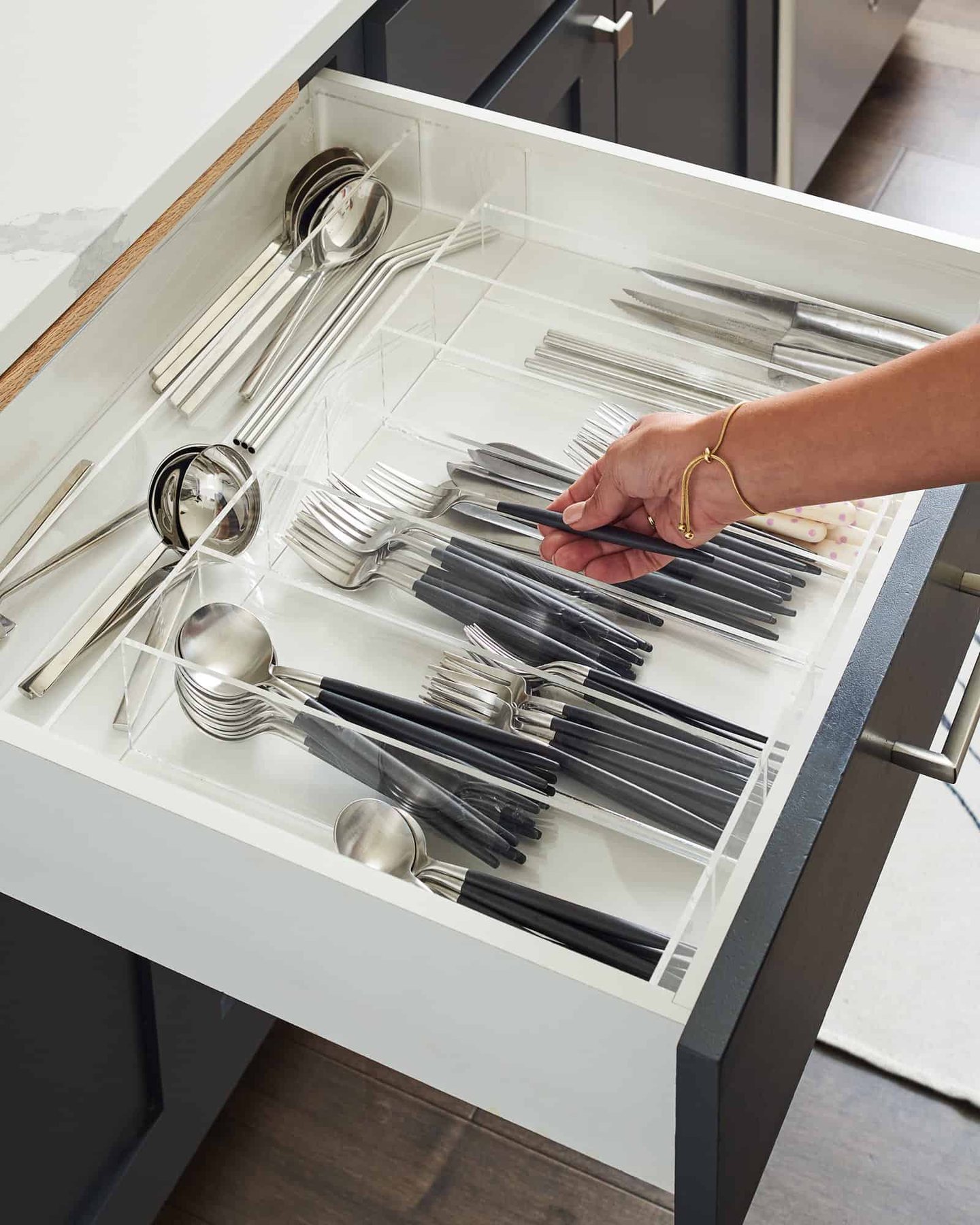 A hand placing a fork in a silverware drawer organized with a custom storage container.
