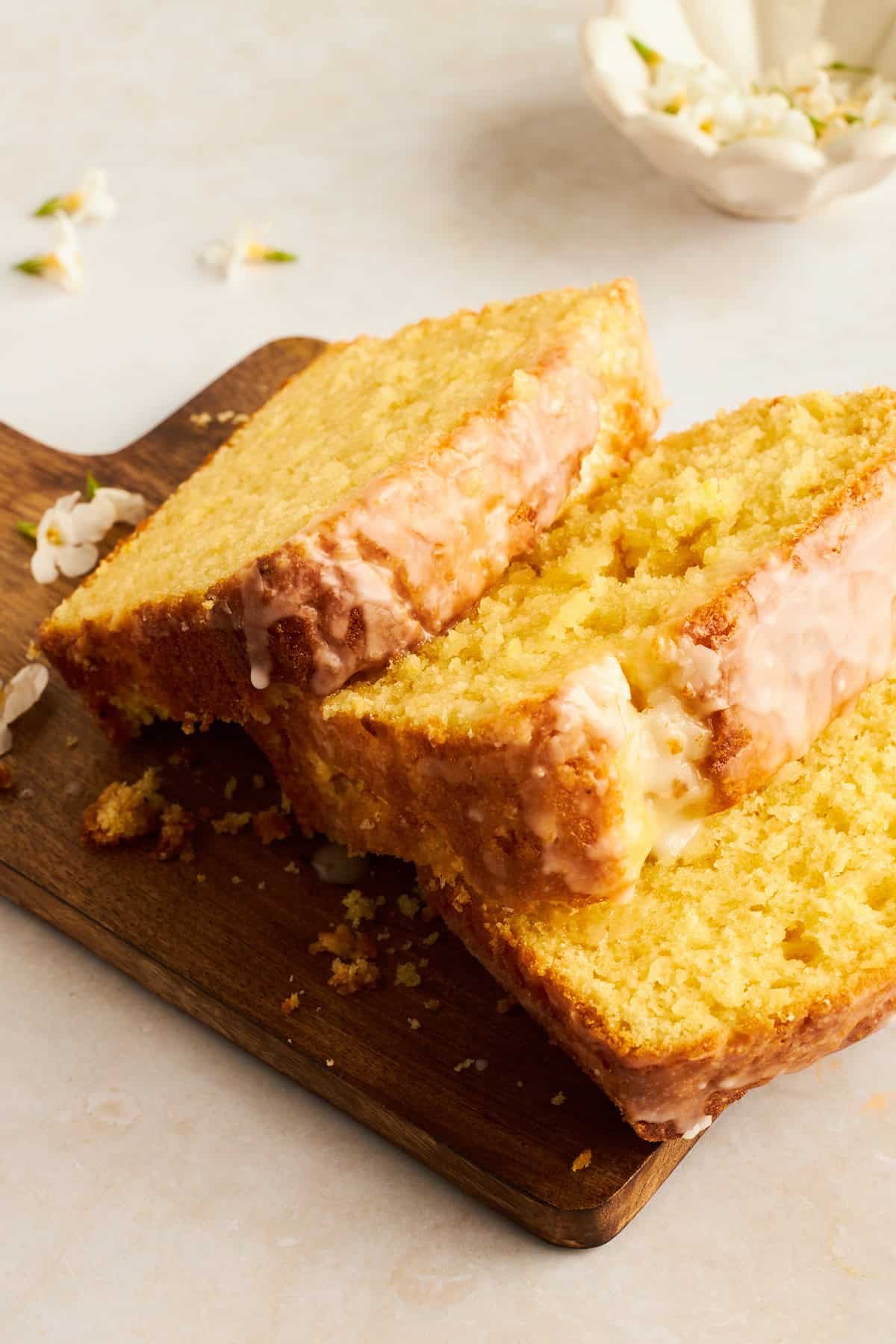 Three slices of glazed lemon bread on a wooden cutting board.