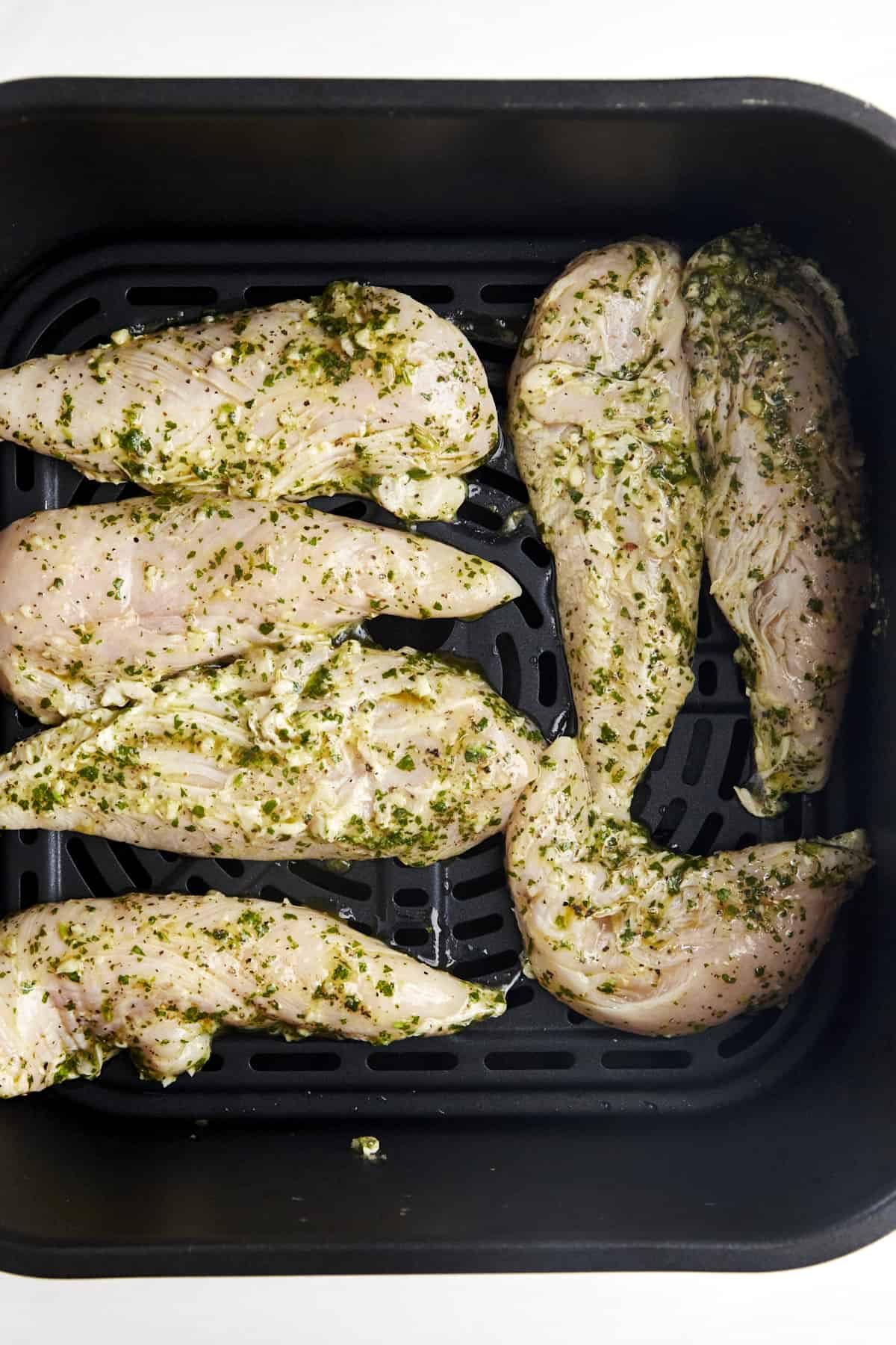 Raw marinaded chicken tenders in an air fryer basket.