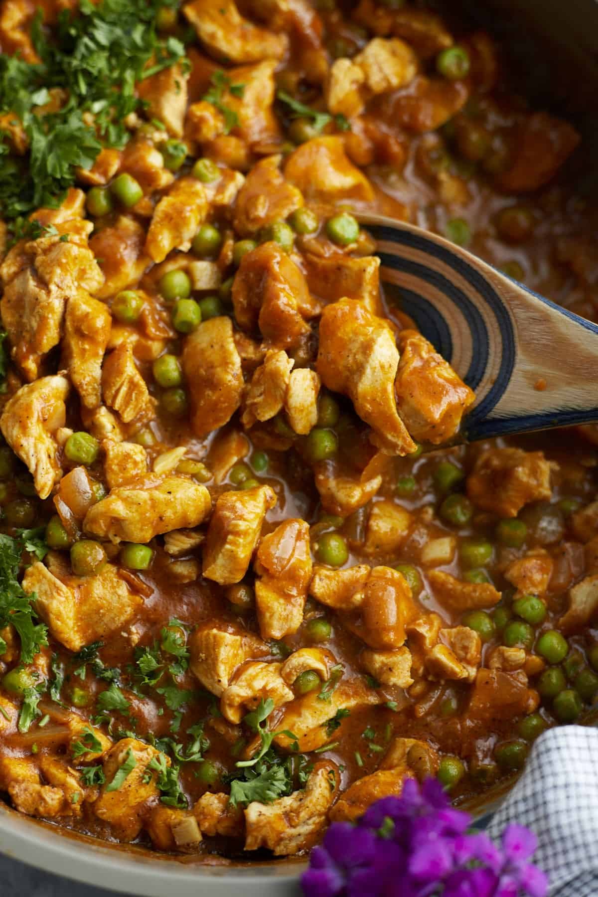 close up image of a wooden spoon stirring madras curry chicken