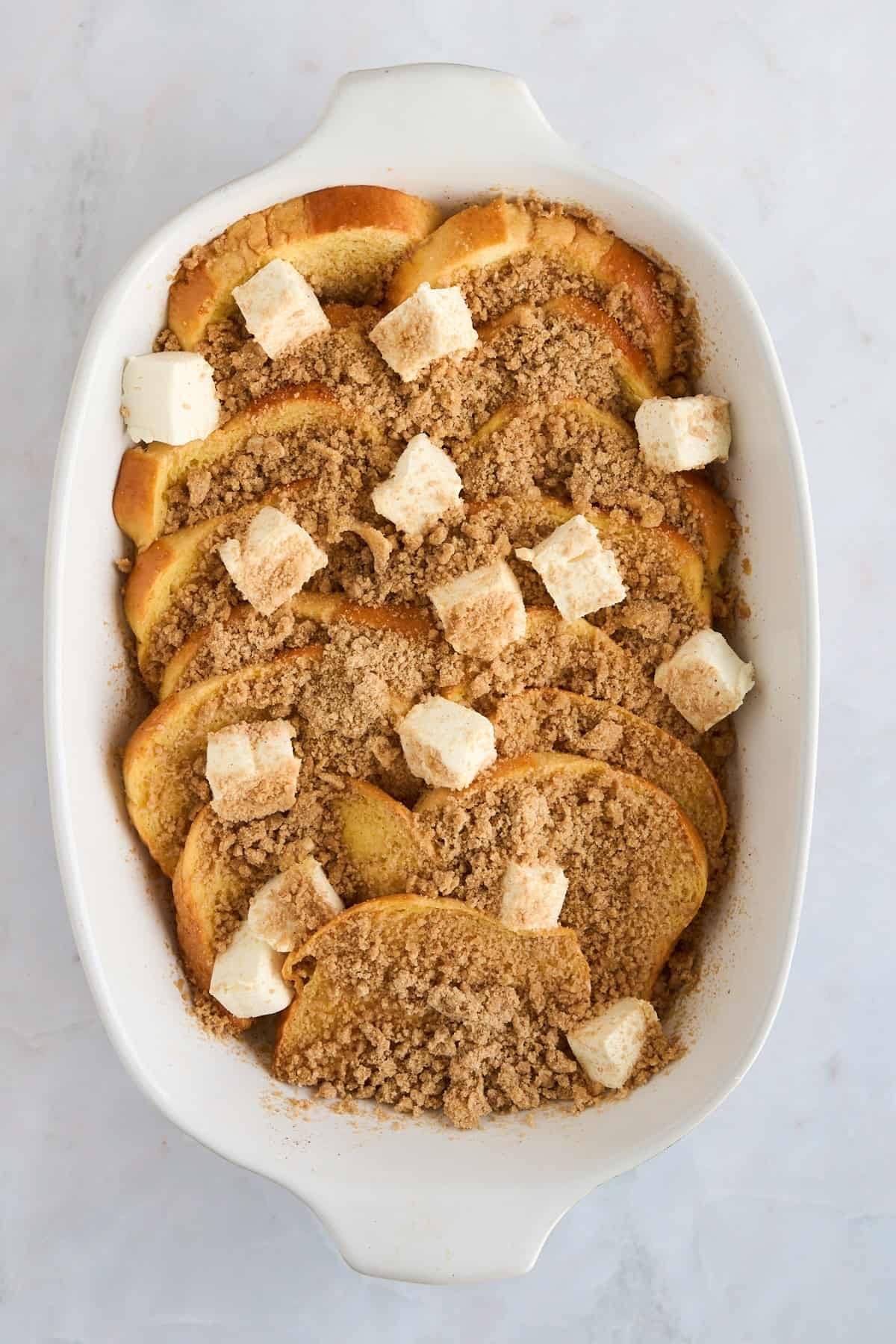 Unbaked maple french toast in a baking dish topped with cream cheese.