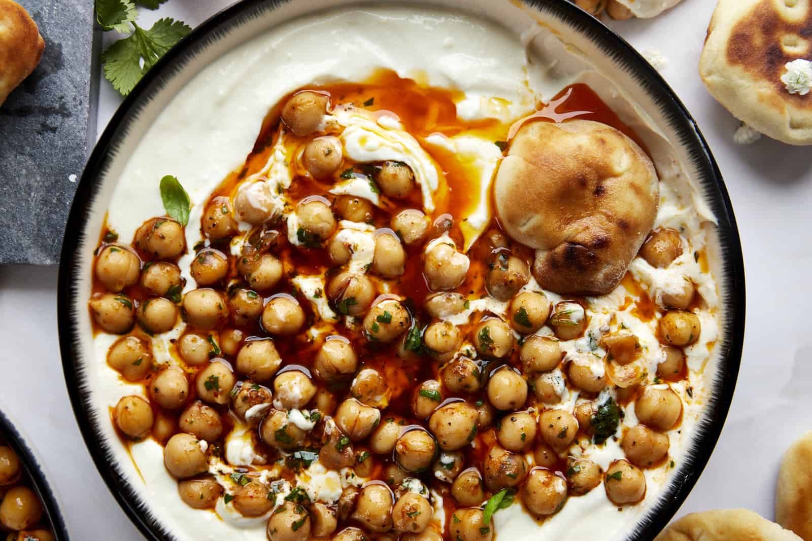 A bowl of whipped feta topped with marinated chickpeas with a piece of bread on top.