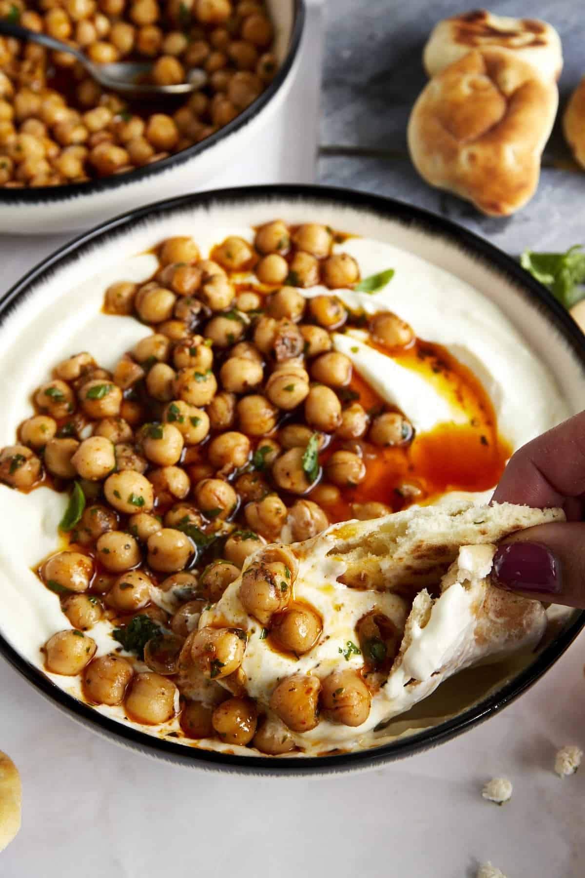 Pita bread being dipped into a bowl of whipped feta topped with marinated chickpeas.