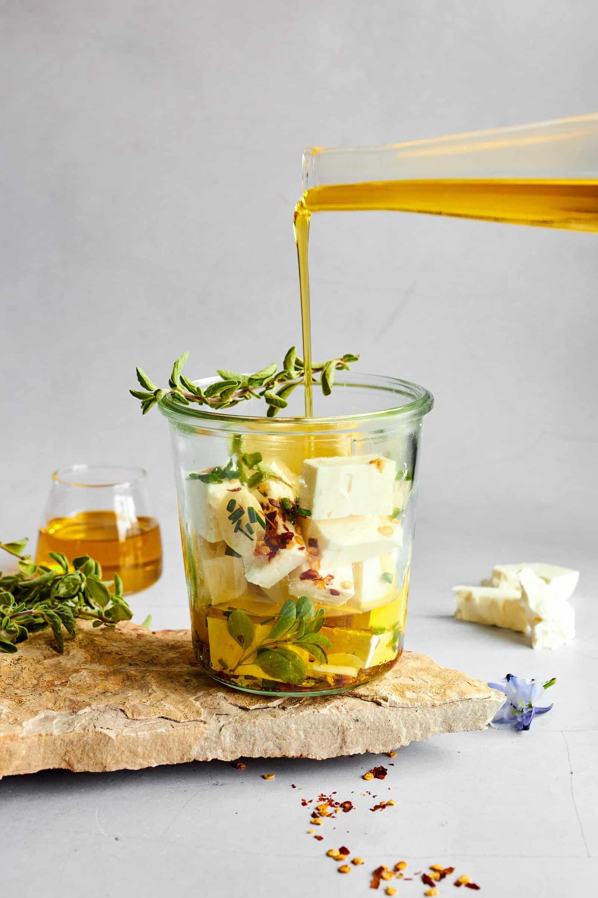 Marinade being poured over feta cubes in a glass container.