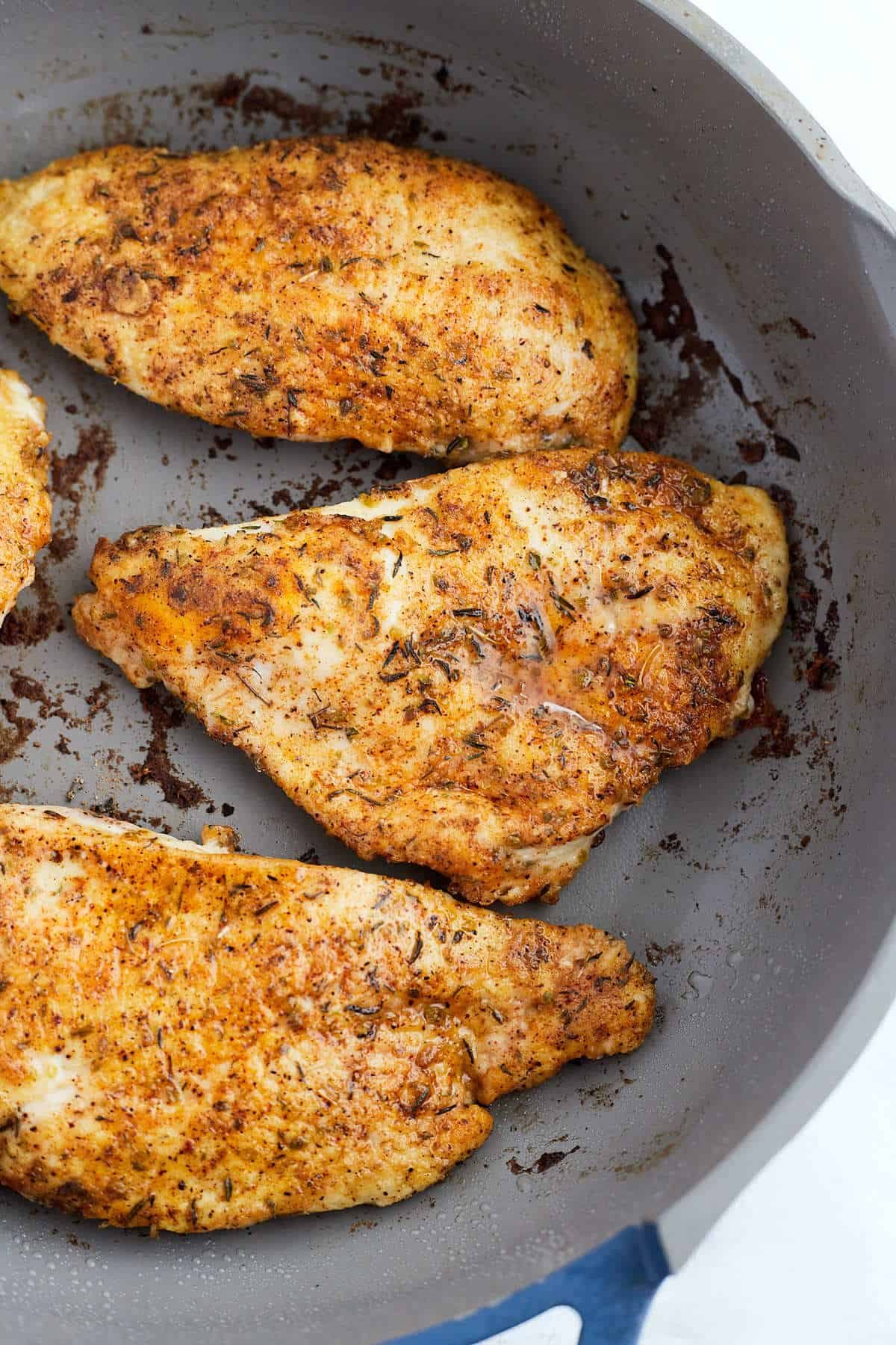 Seasoned chicken being seared in a skillet.