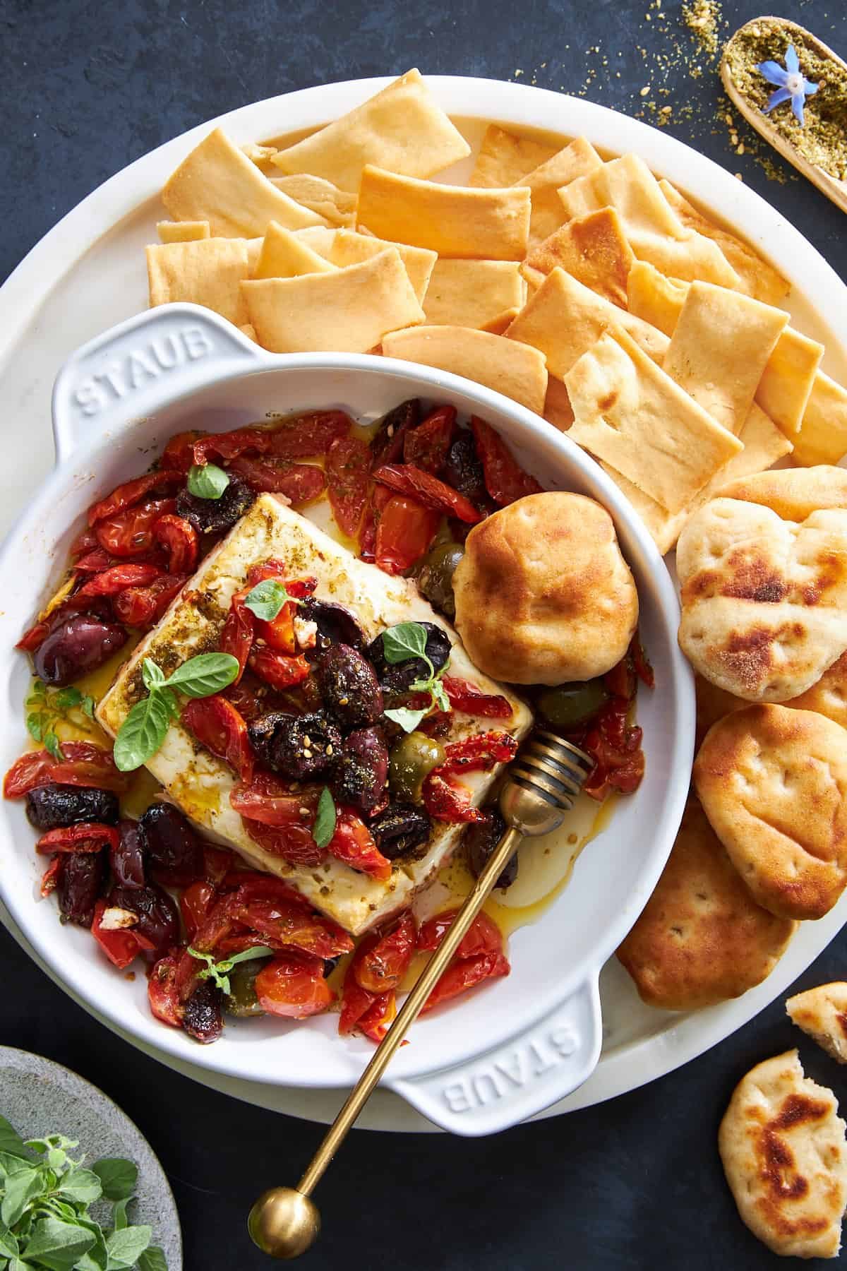 A bowl of Mediterranean baked feta dip surrounded by pita chips and puffs.