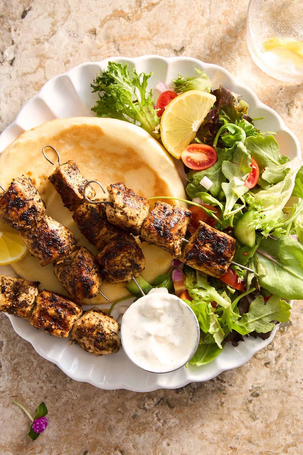 A plate of Mediterranean chicken skewers with pita and salad.