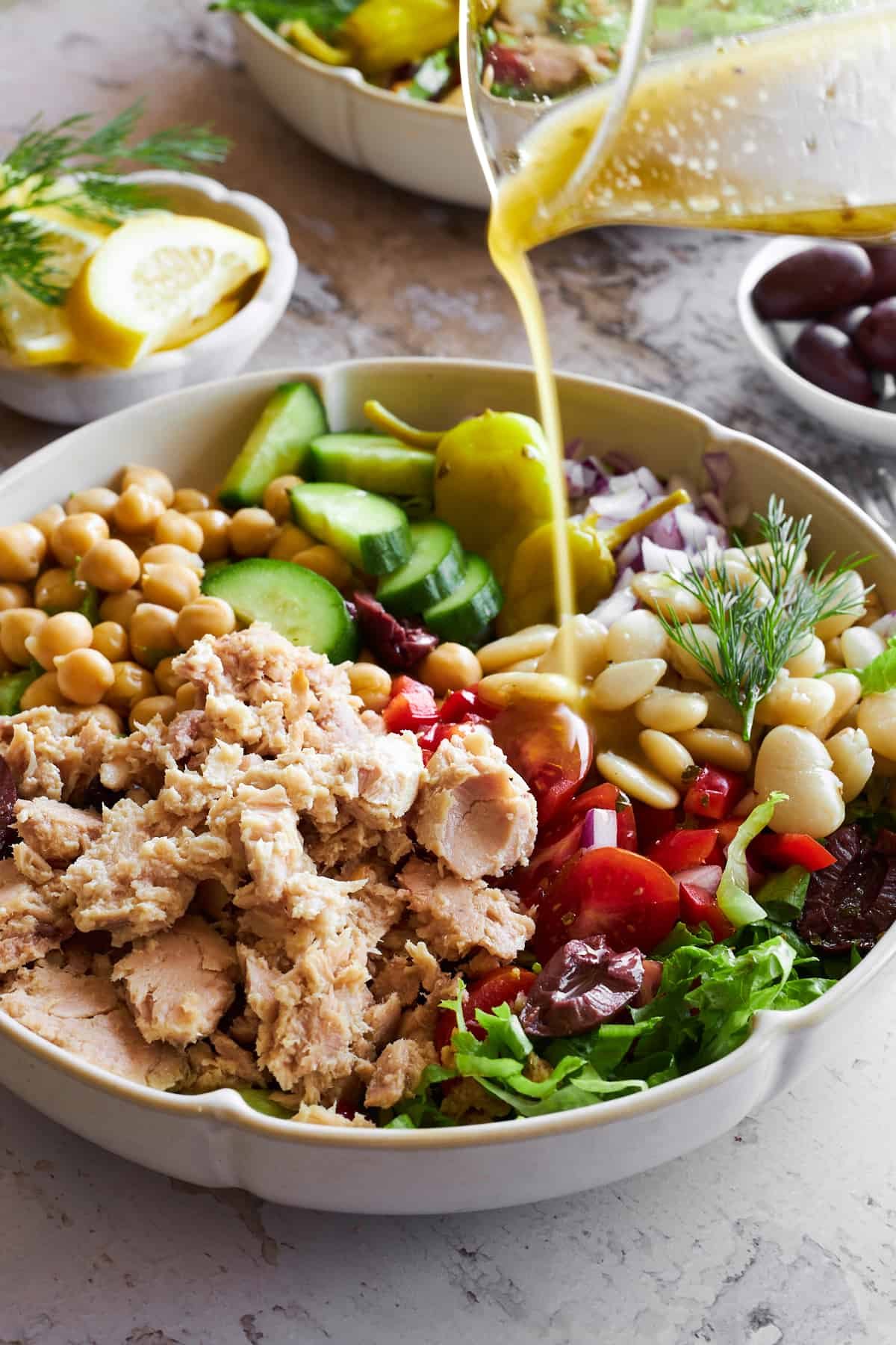 Vinaigrette being poured over a bowl of Mediterranean tuna salad.