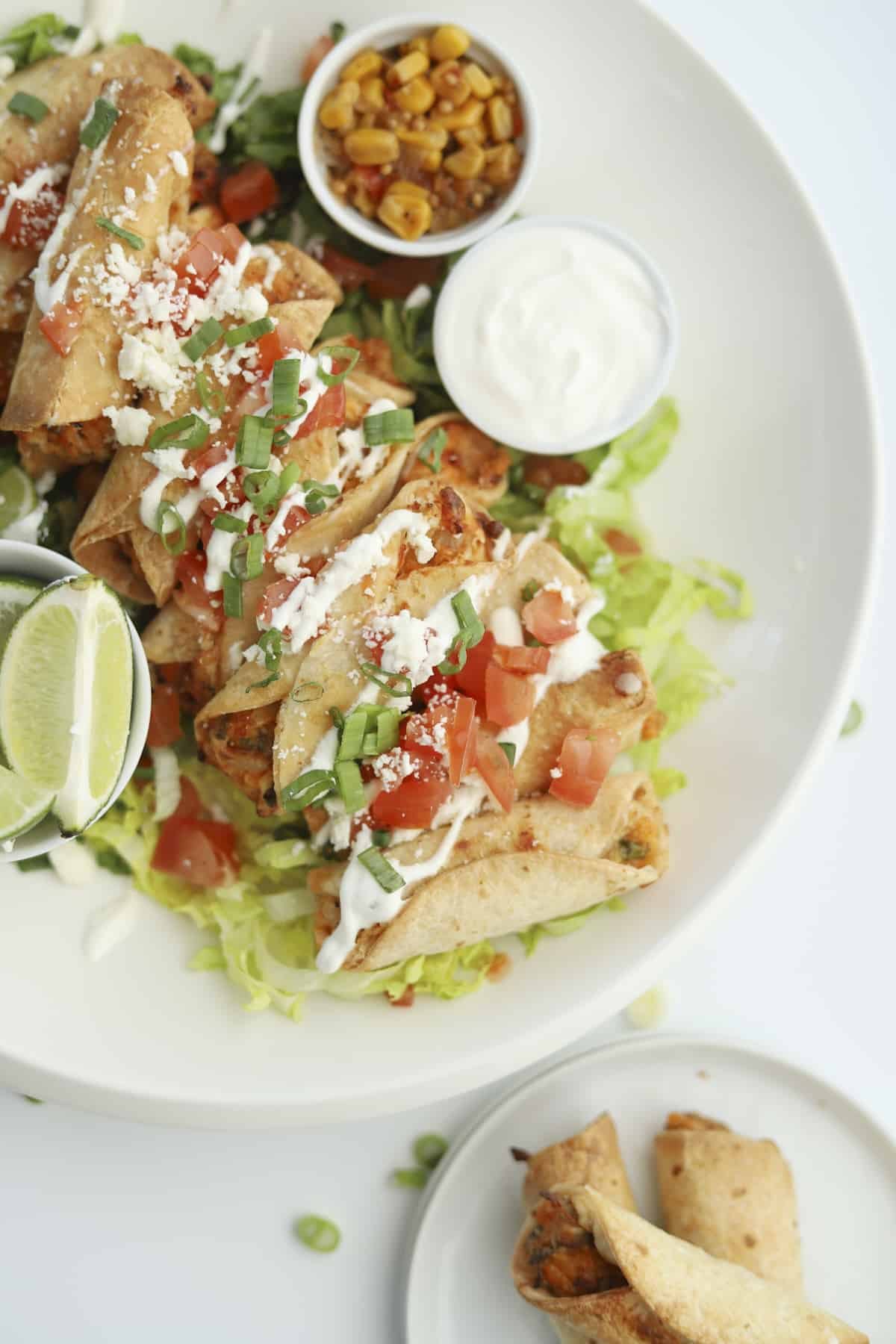 overhead of mini air fryer taquitos with tomatoes, sour cream, and green onions