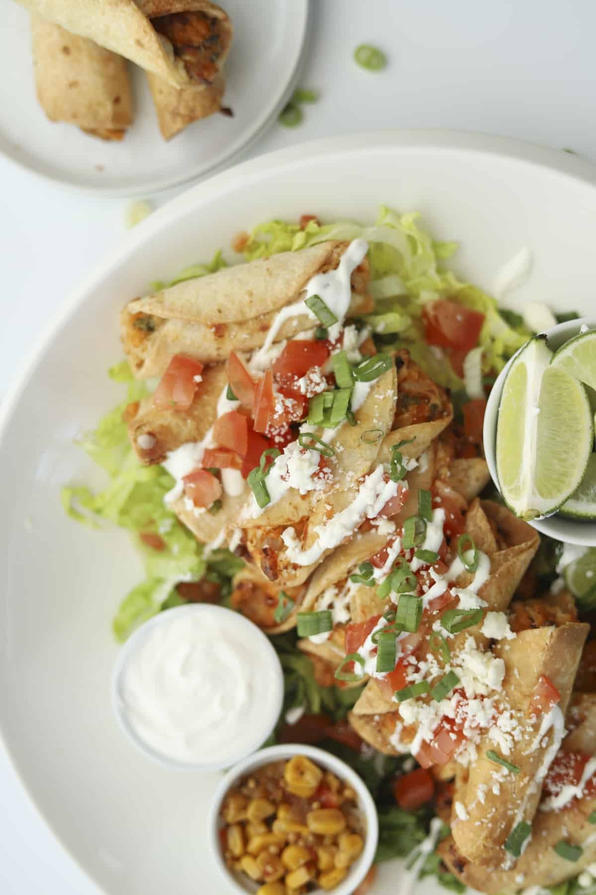 overhead of taquitos garnished with tomatoes, sour cream and limes