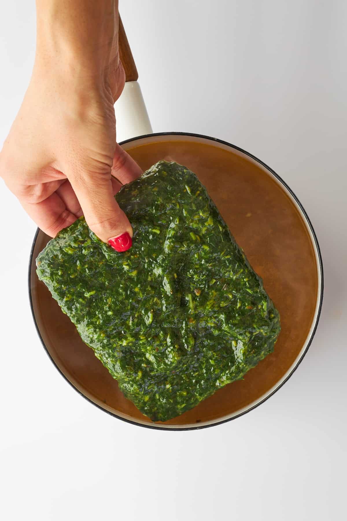 Frozen mulukhiya leaves being added to a pot.