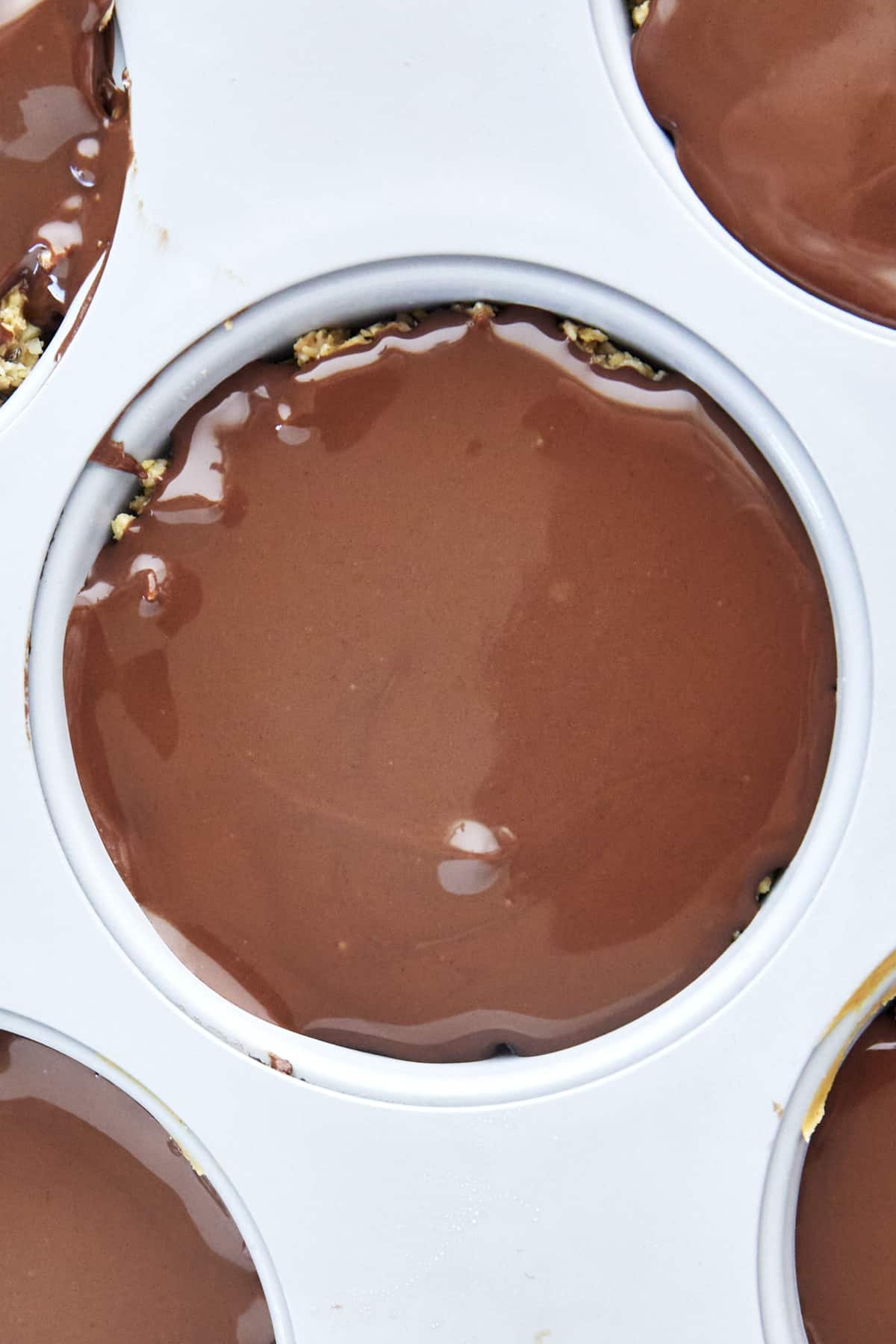 Chocolate covering a no bake peanut butter oat cup in a muffin pan.