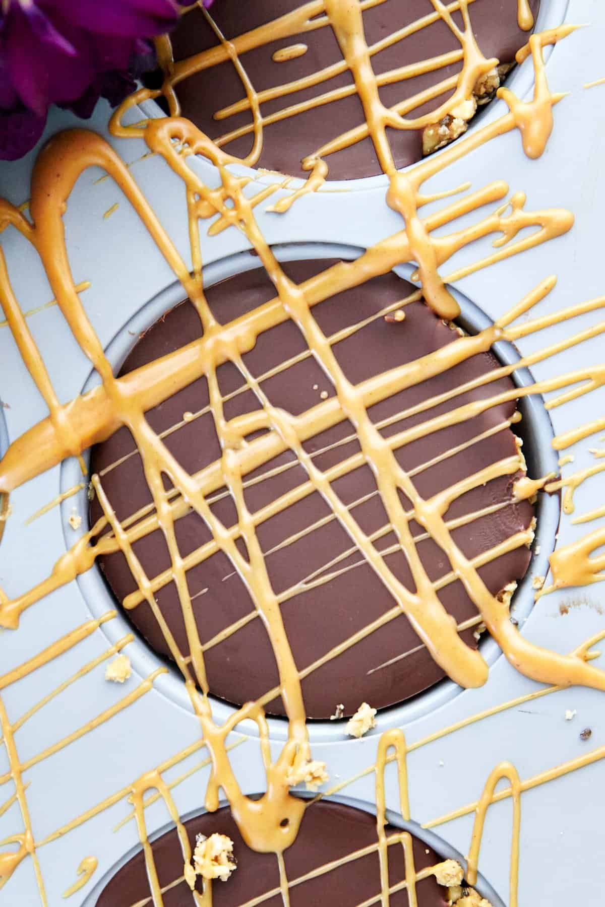 Peanut butter drizzled over a no bake peanut butter oat cup in a muffin pan.