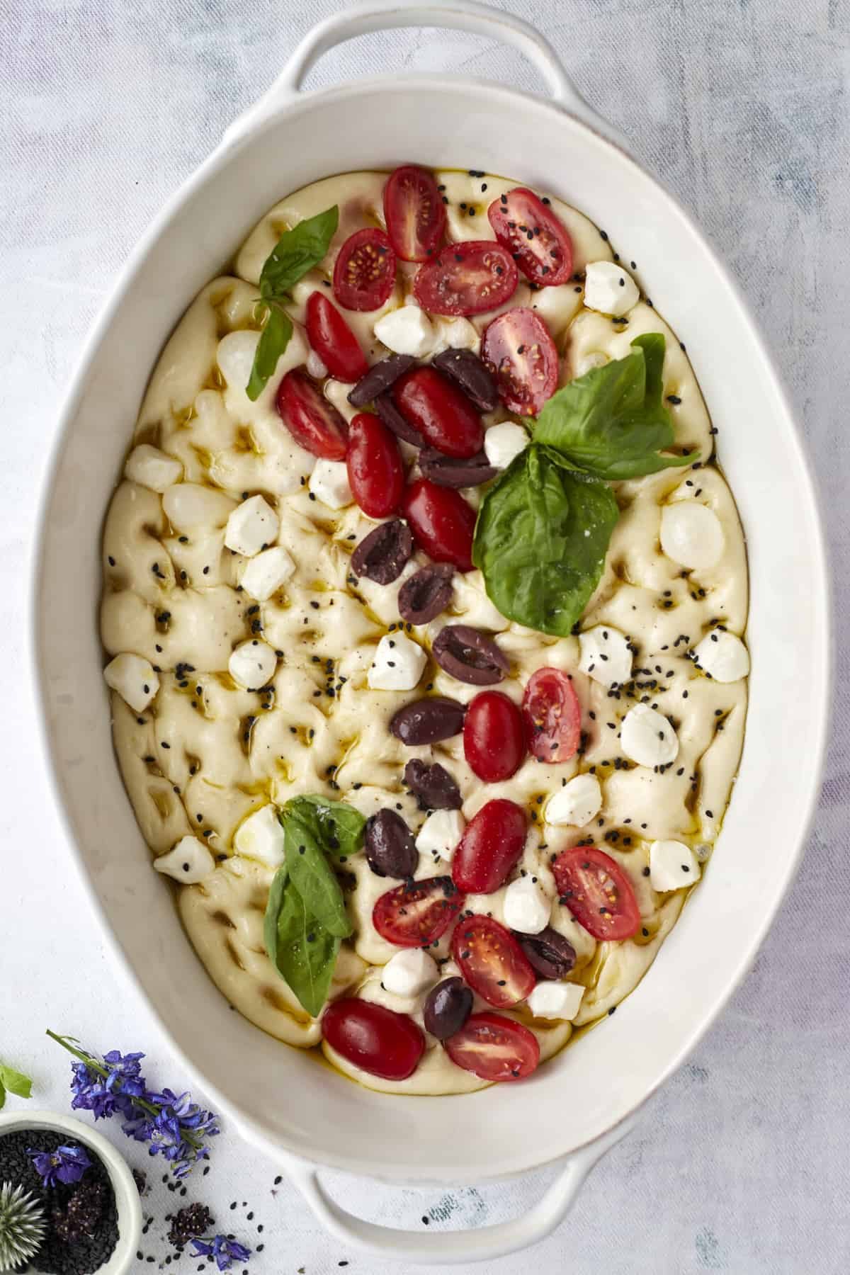 unbaked no knead focaccia bread topped with tomatoes, olives, fresh herbs, and mozzarella