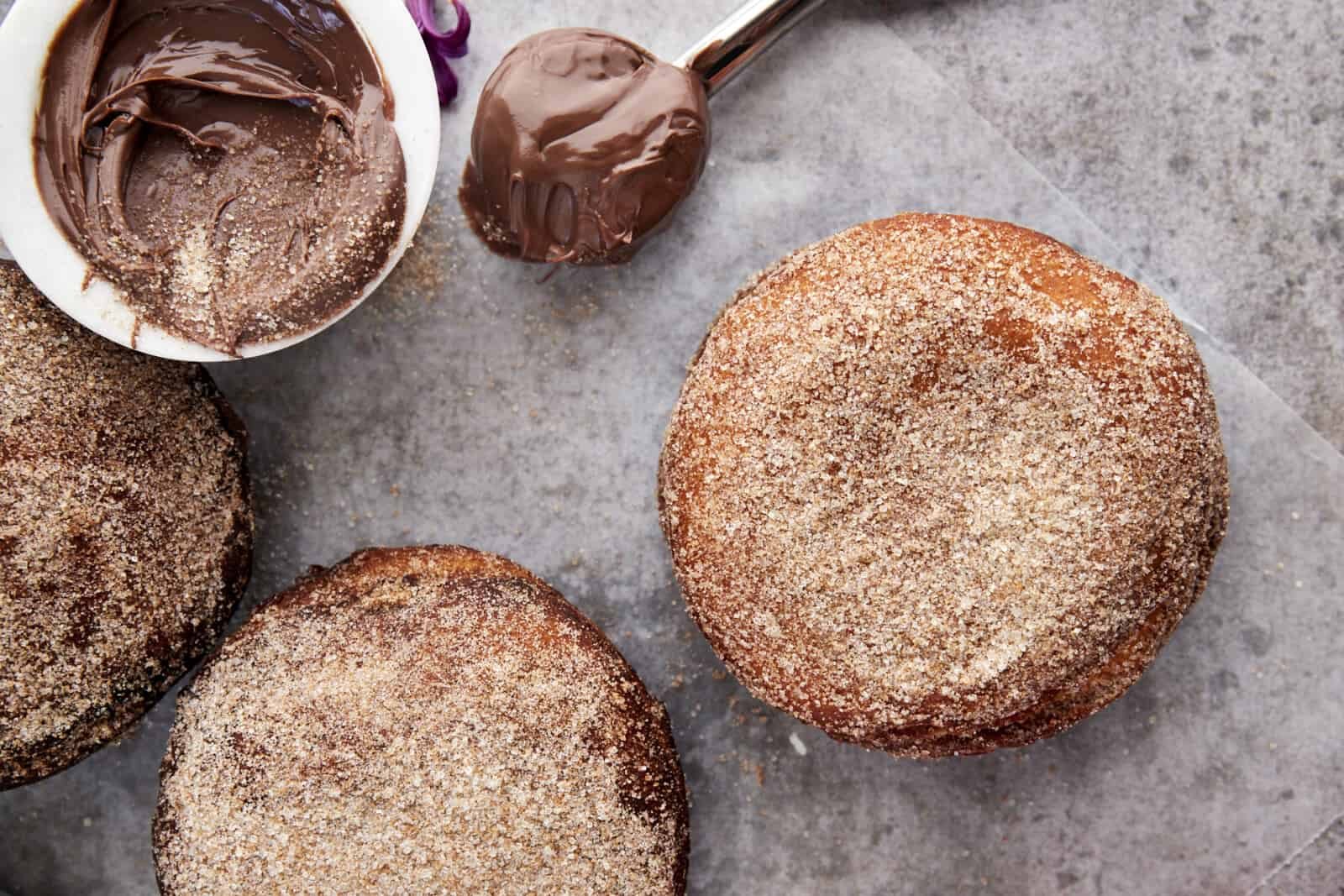 Overhead image of 3 Nutella doughscuits coated with cinnamon sugar with a bowl of Nutella next to them.