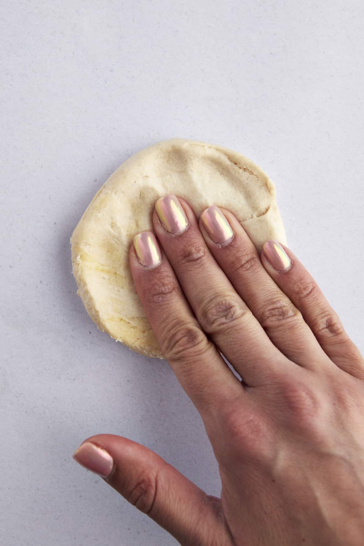 Raw biscuit dough being flattened into a disc.