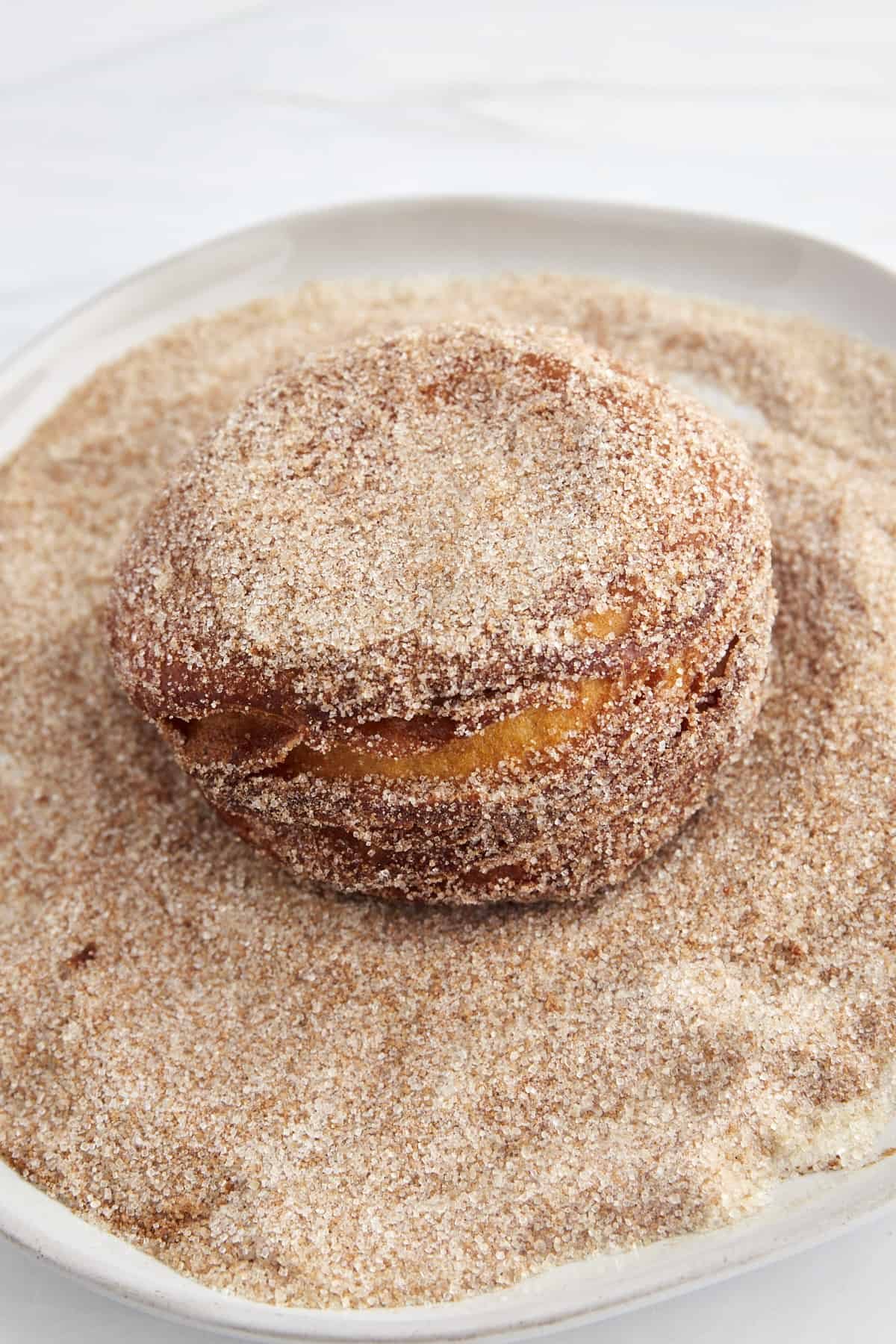 A Nutella stuffed biscuit doughnut in a bowl of cinnamon sugar.