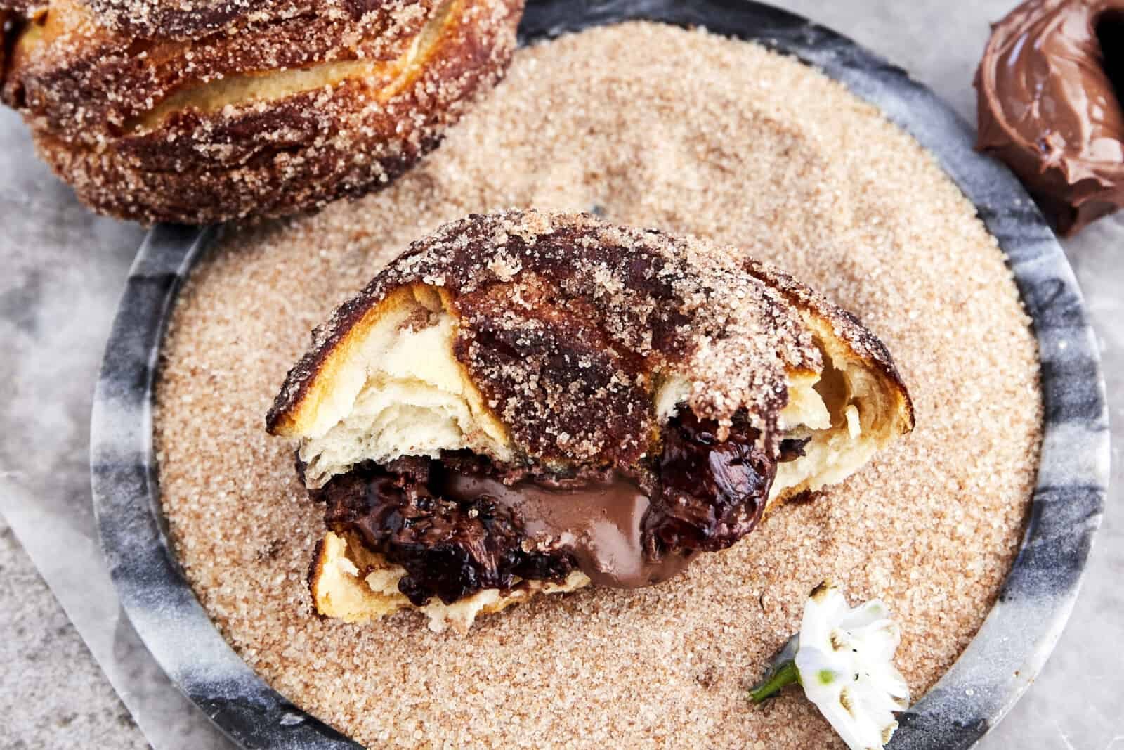 Half a Nutella stuffed biscuit doughnut in a bowl of cinnamon sugar.
