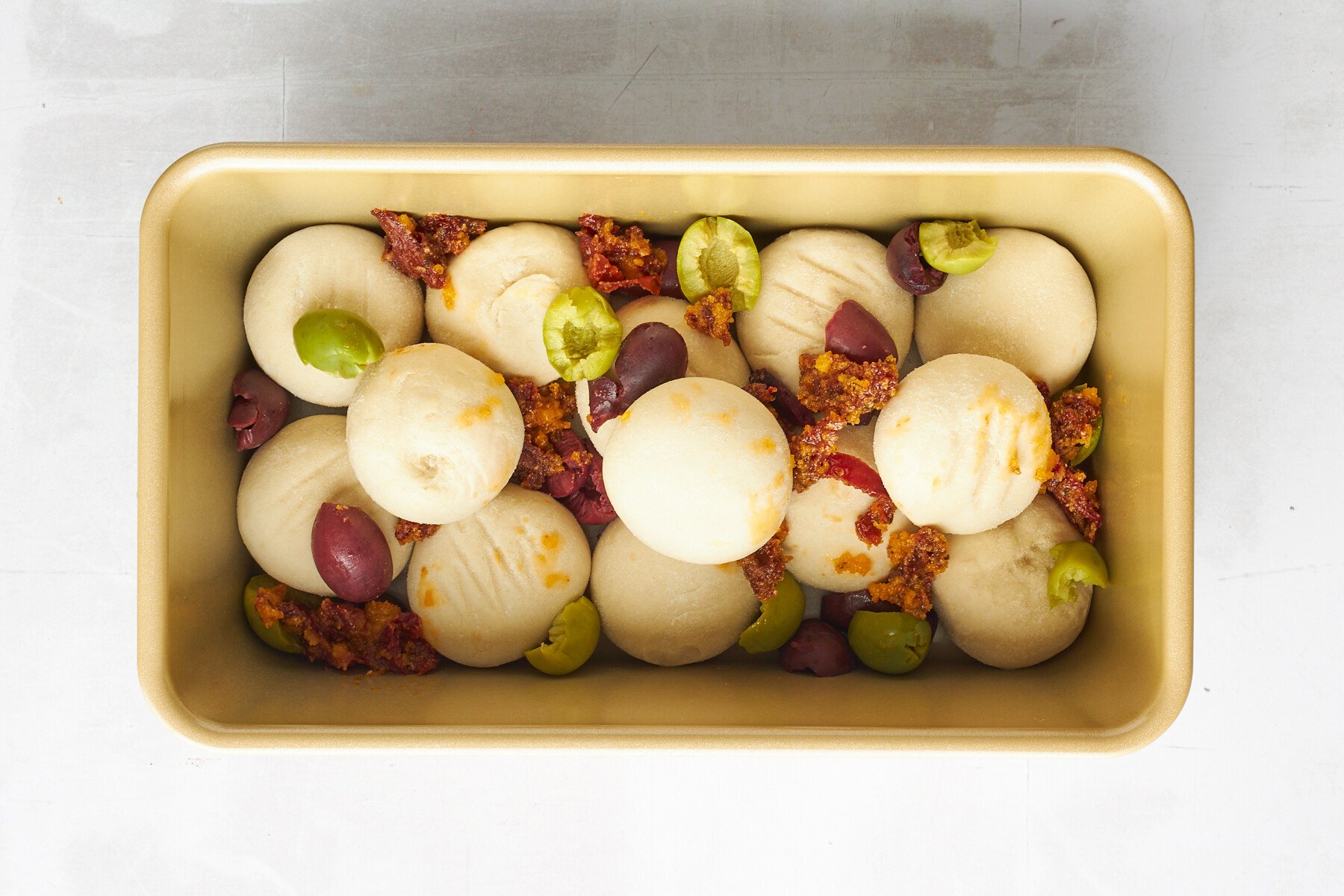 Raw dinner rolls topped with kalamata olives and sun-dried tomatoes.