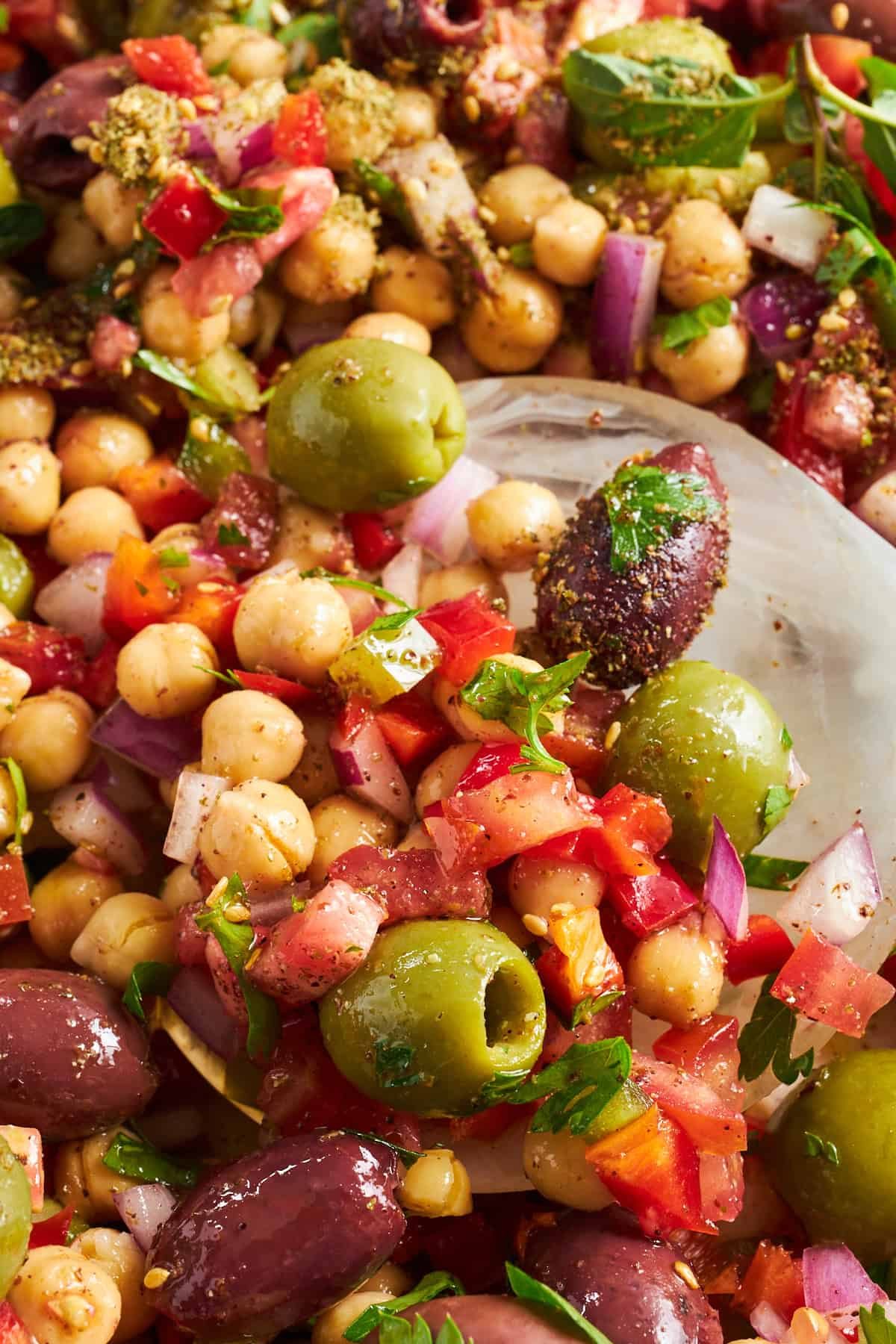 Close up view of olive salad with chickpeas, tomatoes, red onion, and herbs.