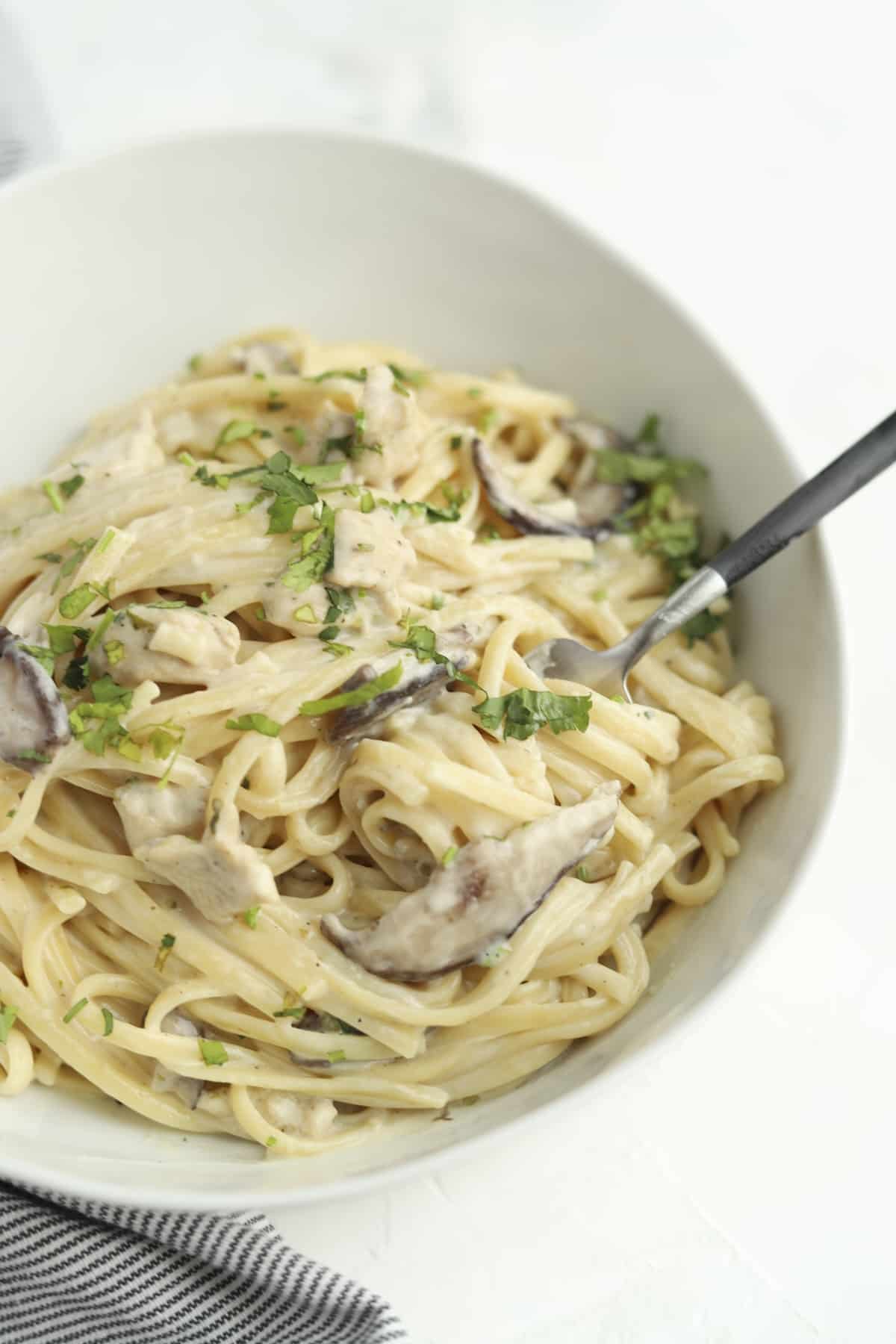 a bowl of chicken tetrazzini topped with herbs with a fork sticking out