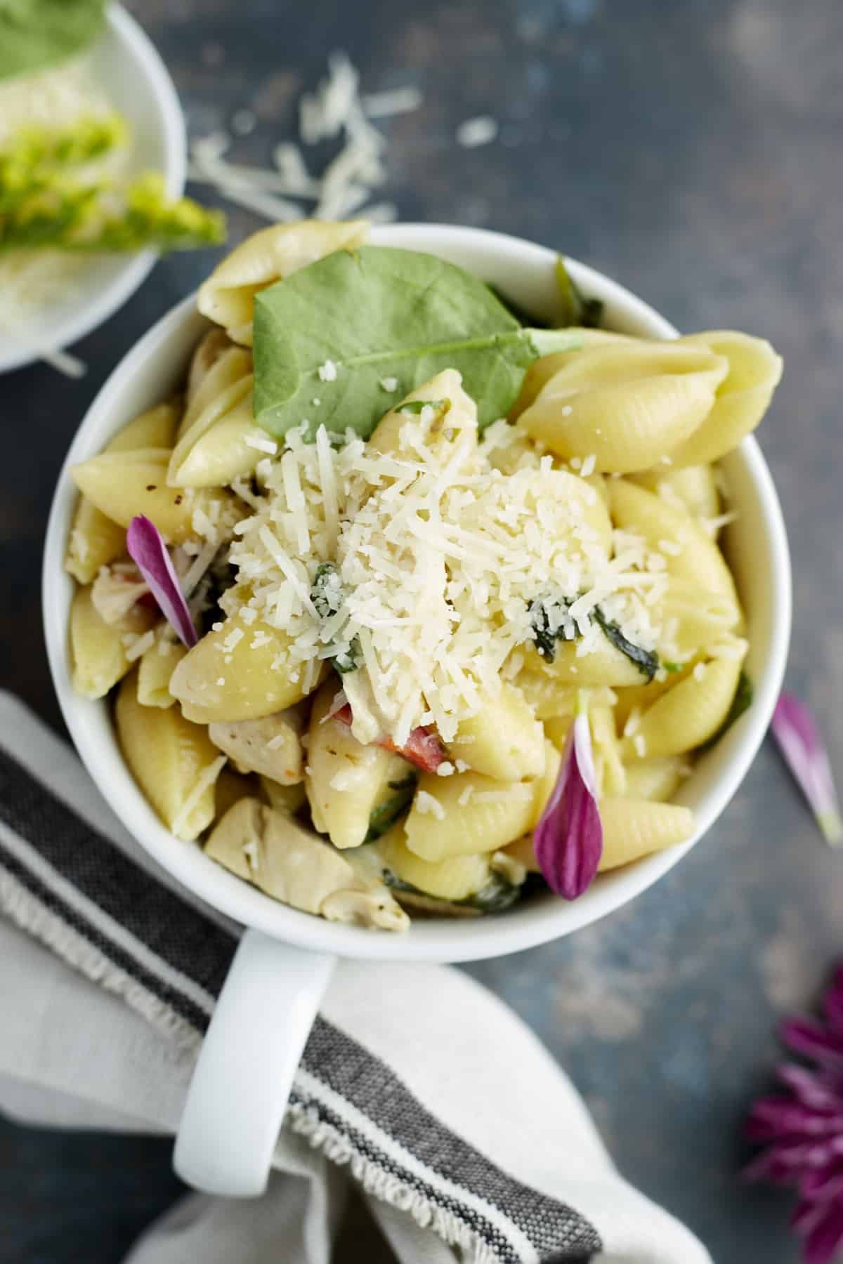 A mug full of silky tuscan chicken pasta topped with grated Parmesan.