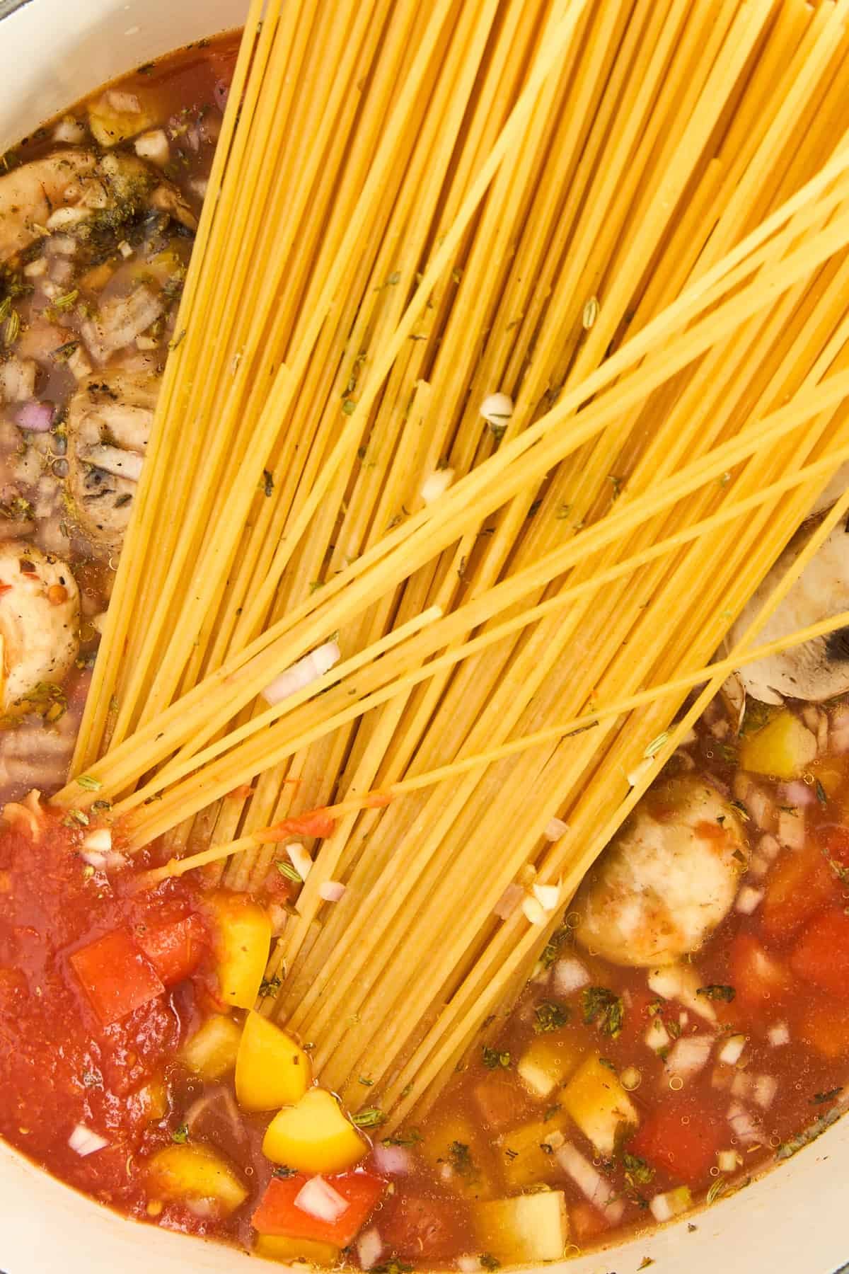 A pot of sautéed veggies, tomato sauce, broth, and raw spaghetti noodles.