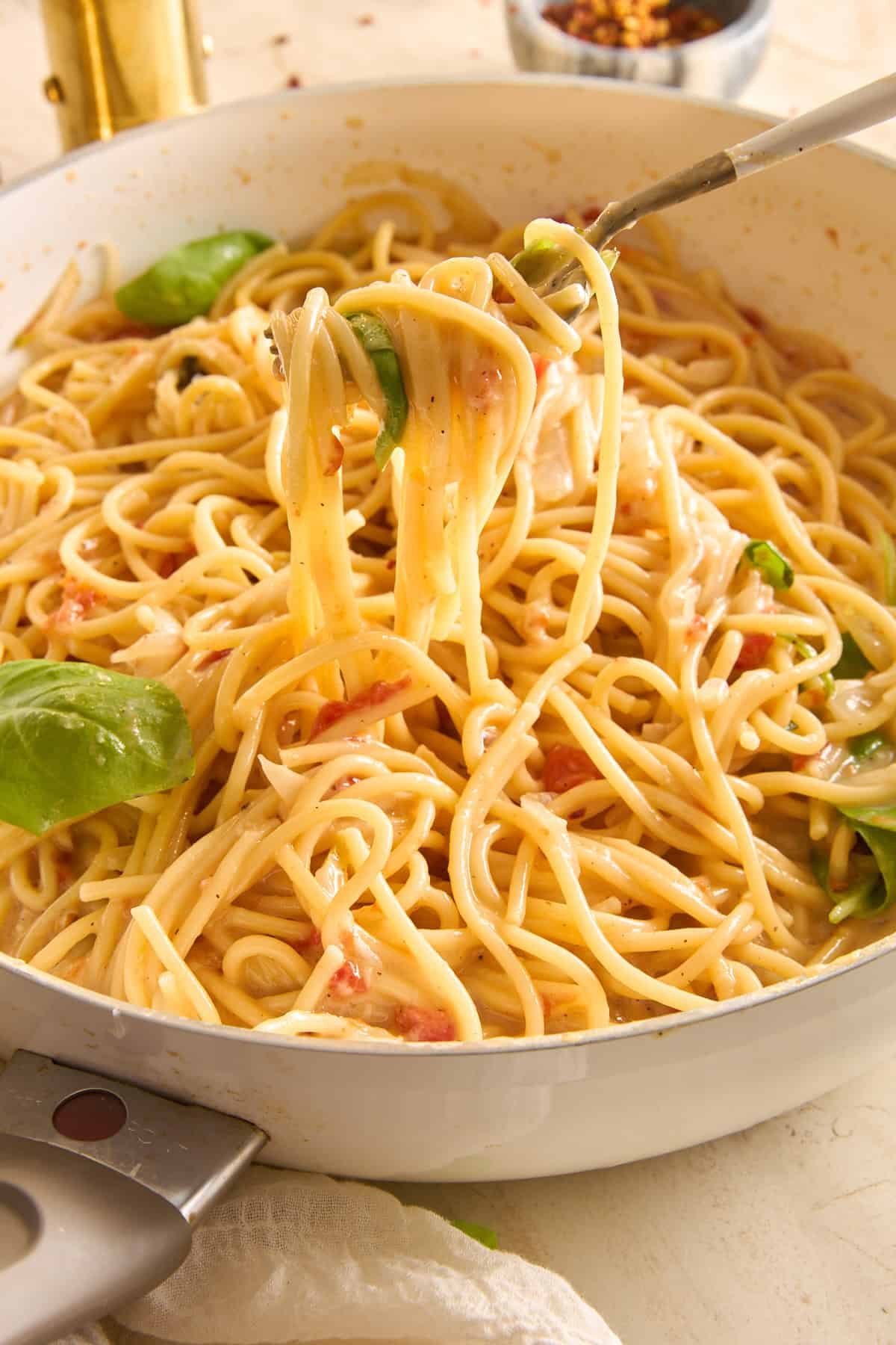 A fork lifts a serving of creamy spaghetti from a white pan, with visible spinach leaves and a light sauce coating the pasta.