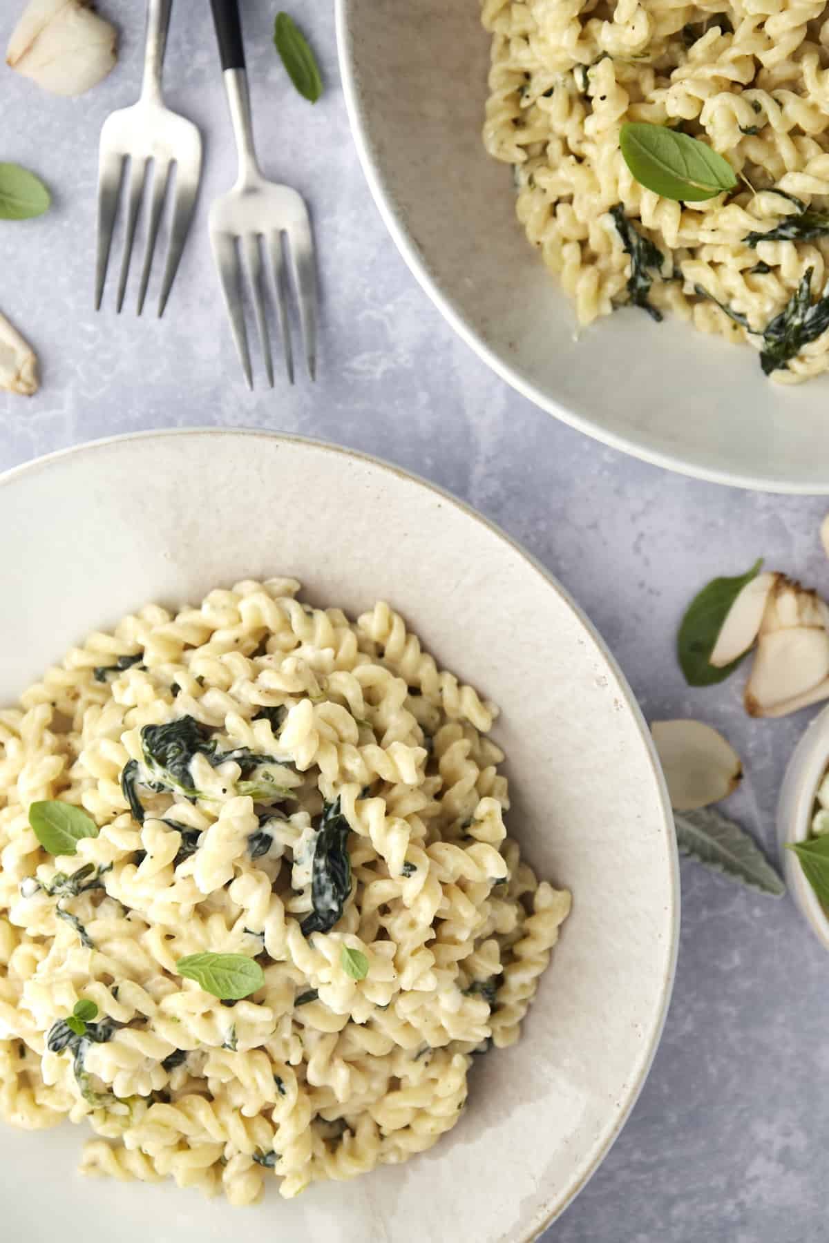 two bowls of Spanakopita Pasta with Spinach with two forks in the upper lefthand corner