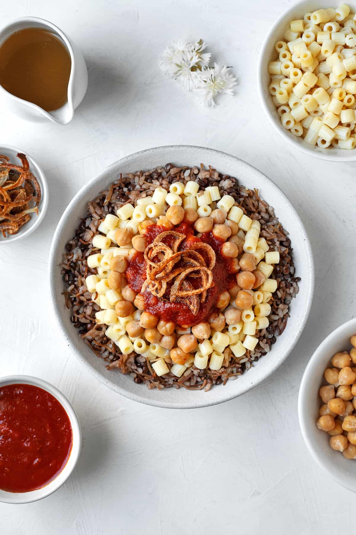 overhead image of a bowl of Egyptian koshari with rice, pasta, chickpeas, tomato sauce, and fried onions